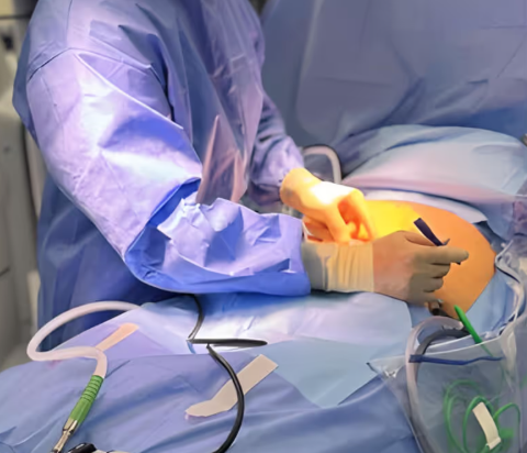 Surgeon in blue scrubs performing an operation on a patient with gloves and medical tools.