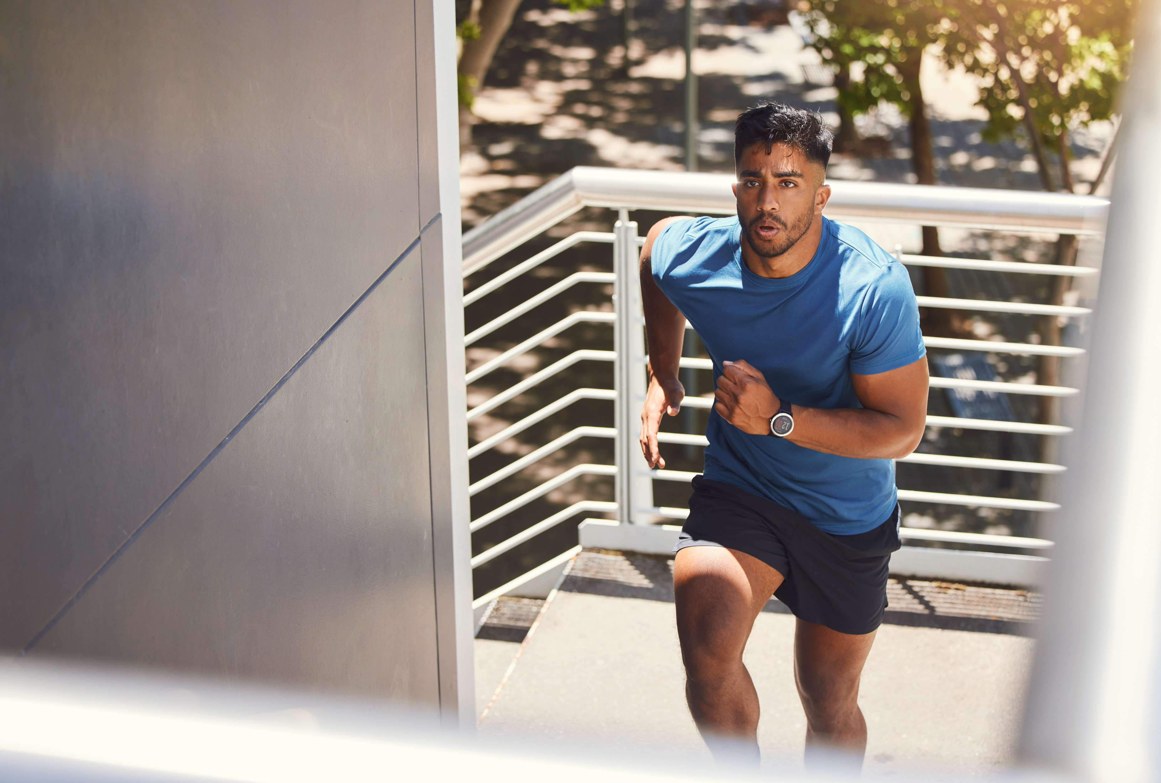 Young man in blue shirt and black shorts running up outdoor stairs on a sunny day.