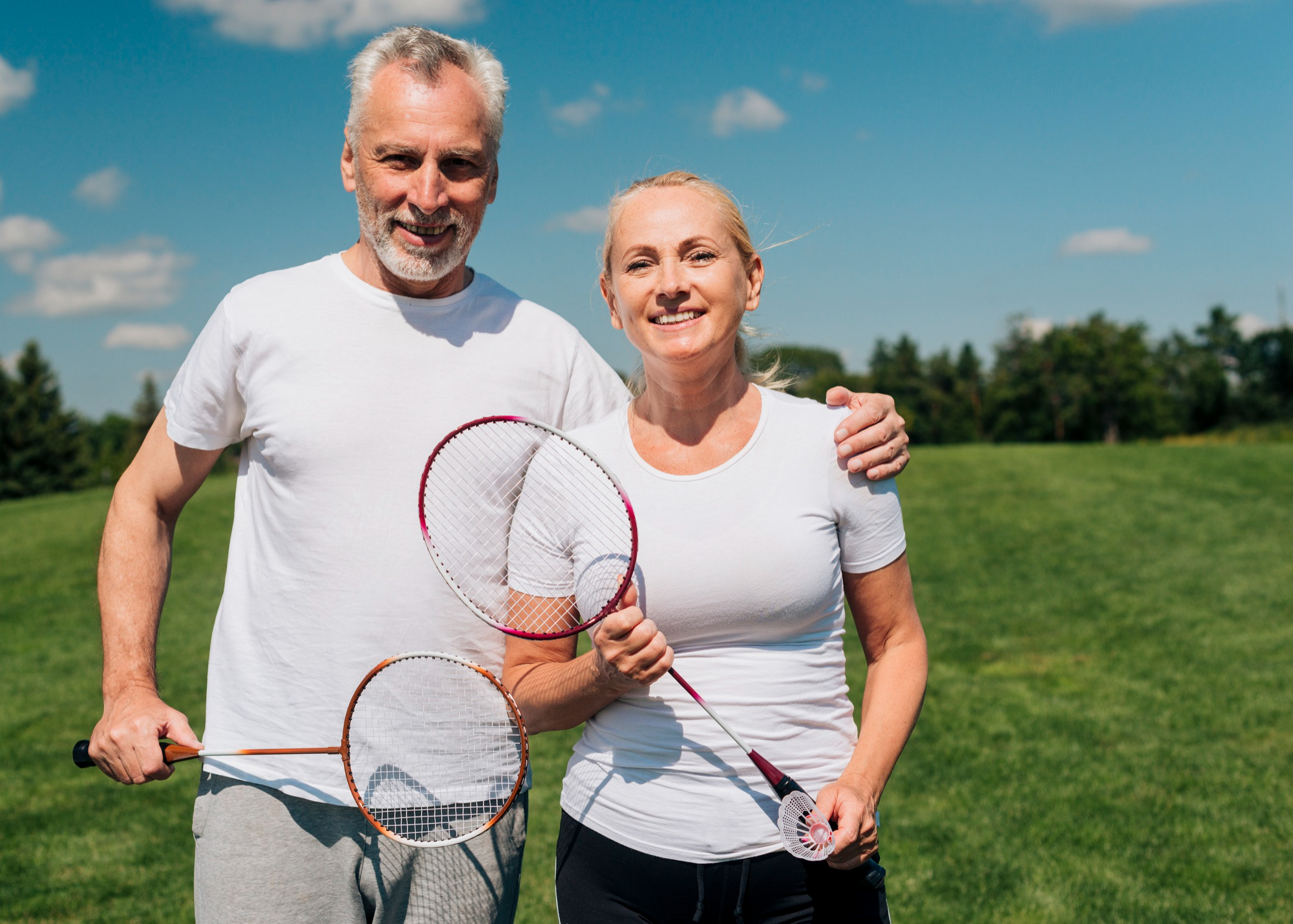 Active older couple holding badminton rackets outdoors, longevity medicine patients at Lifetime Performance Medicine in Los Gatos