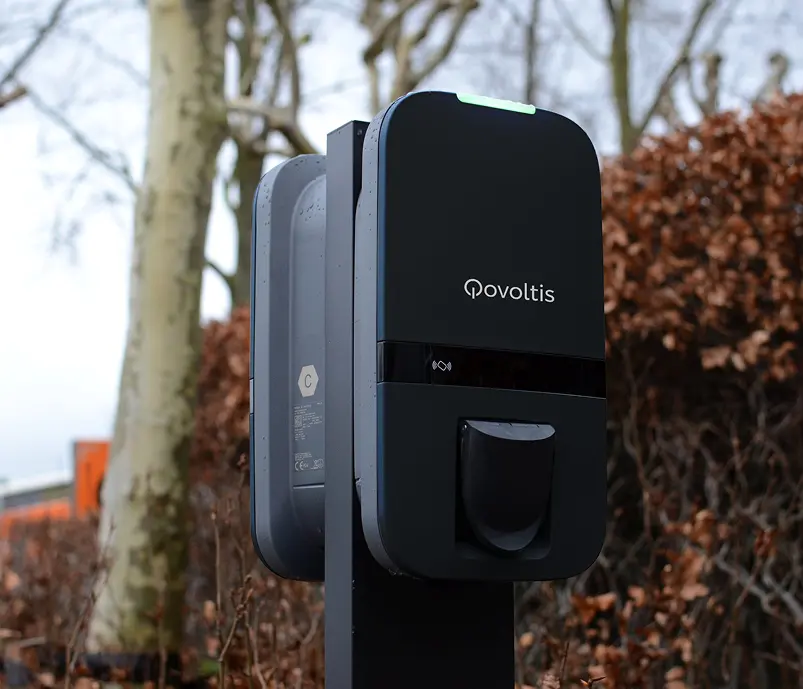 Borne de recharge extérieure Qovoltis sur pied, installée devant un hôtel