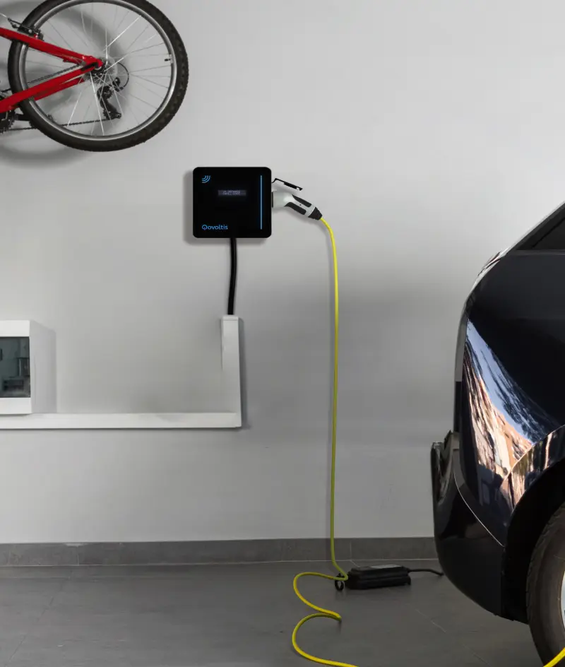 Véhicule électrique en charge la nuit sur une Qobox mini installée devant une maison