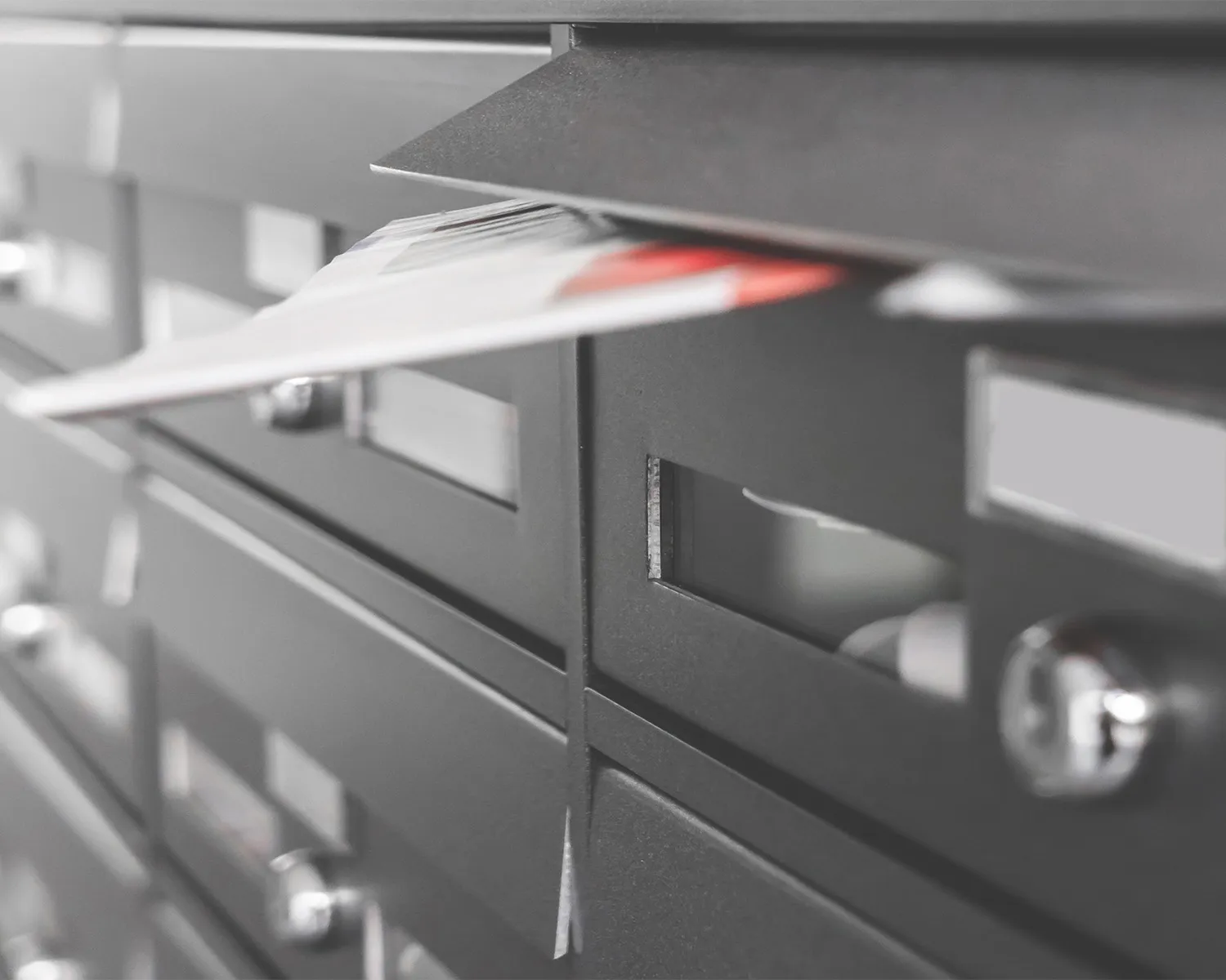 Stacked black metal mailboxes with a leaflet partially inserted in one mailbox.