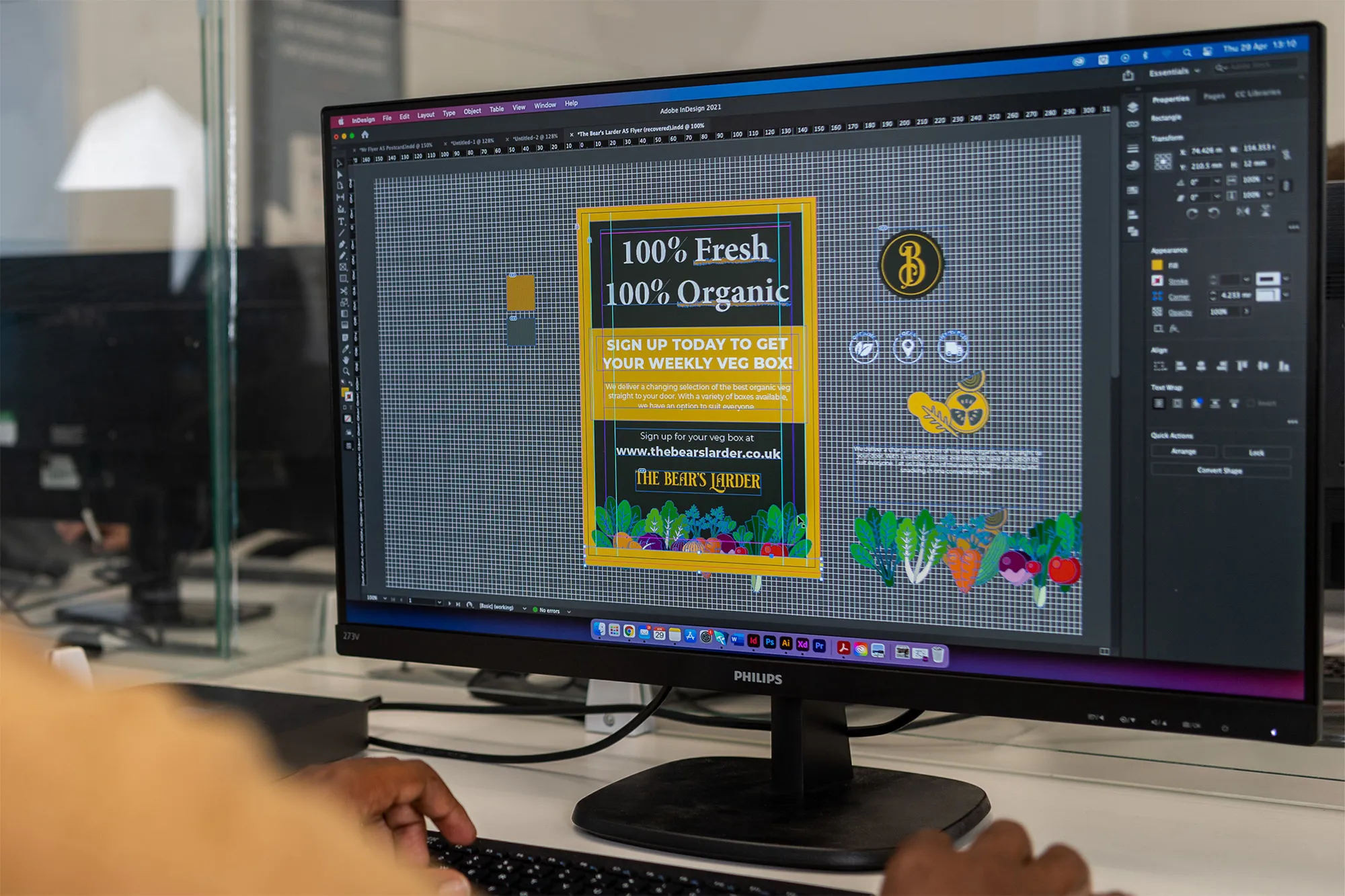 Computer monitor displaying Adobe InDesign with a flyer design for a weekly organic vegetable box service called The Bear's Larder.