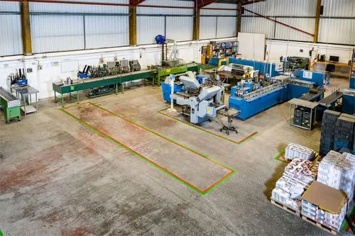 Wide industrial workshop with machinery, workbenches, and stacks of materials on a concrete floor.