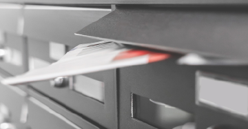 Close-up of a black mailbox with a partially inserted white and red envelope.