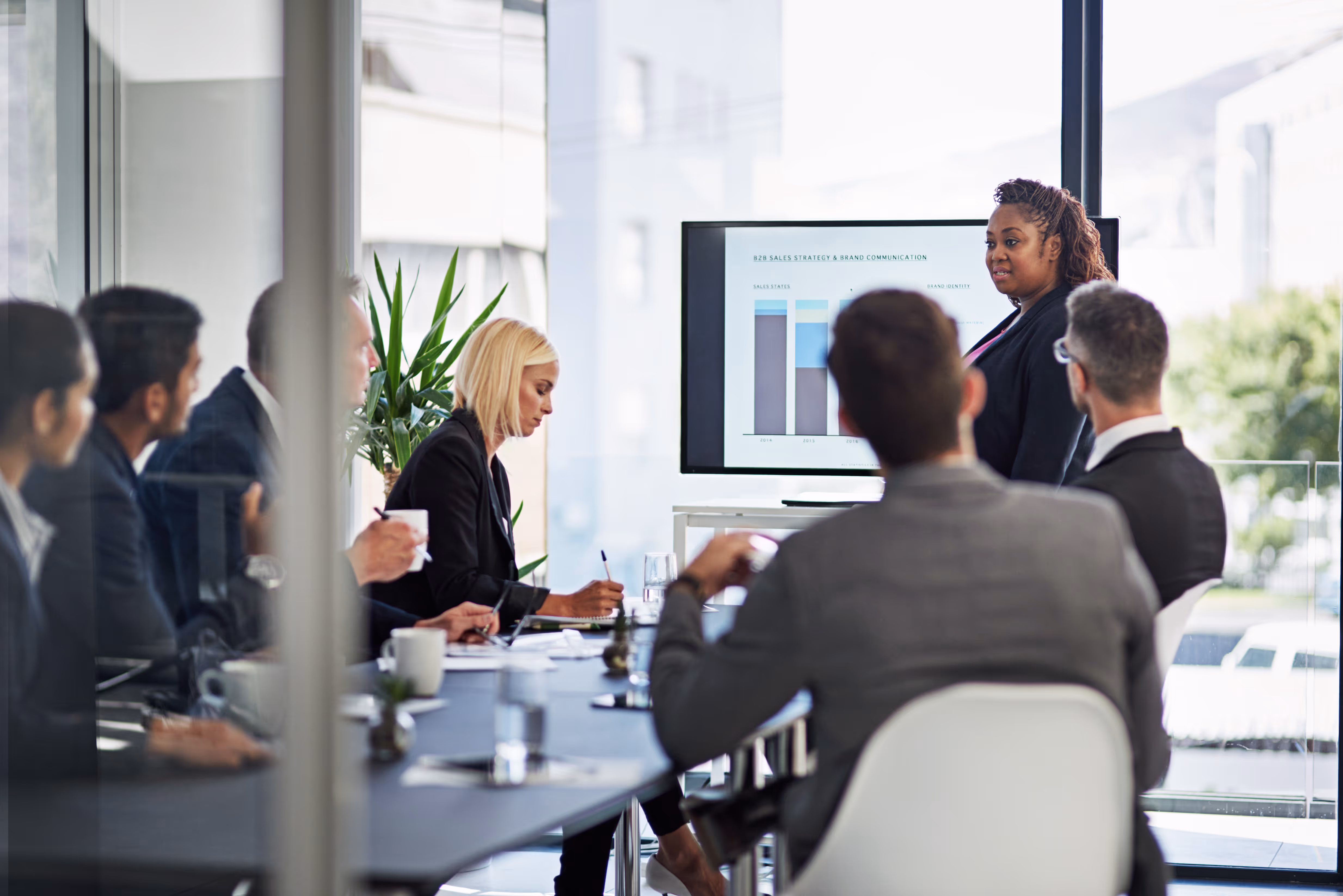 Eine Person präsentiert Inhalte auf einem Bildschirm in einem Besprechungsraum mit mehreren Personen