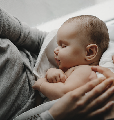 A sleeping baby cradled in a person's arms, with a peaceful expression and soft, light-colored skin.
