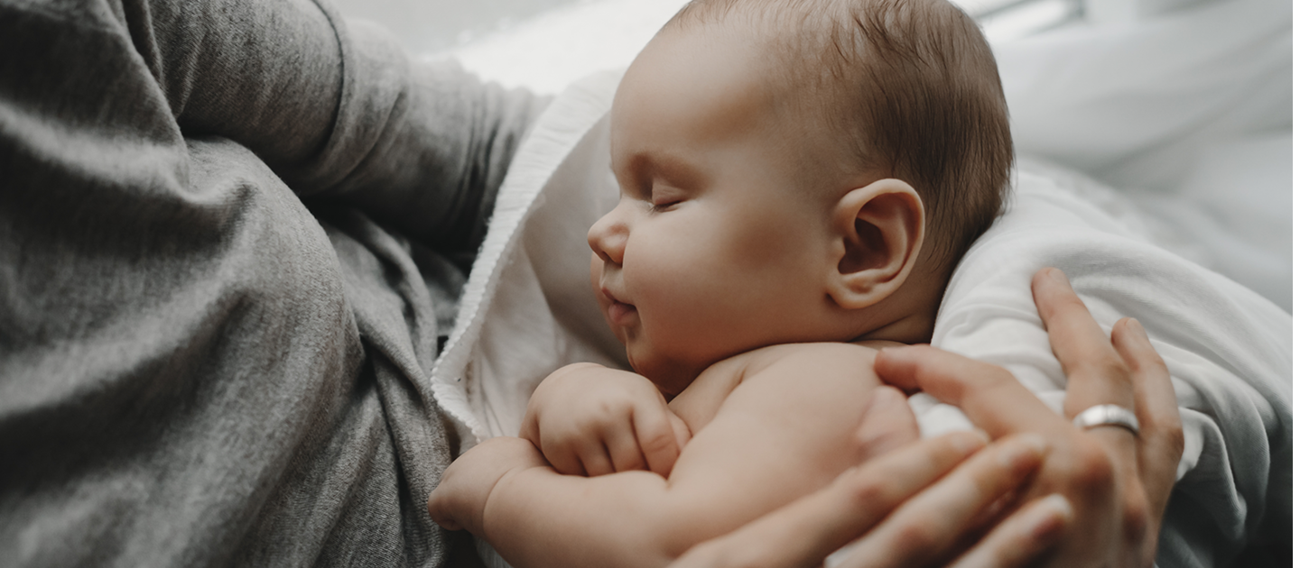 A close-up of a peaceful sleeping baby cradled in a person's arms, with the baby's eyes closed and a content expression.