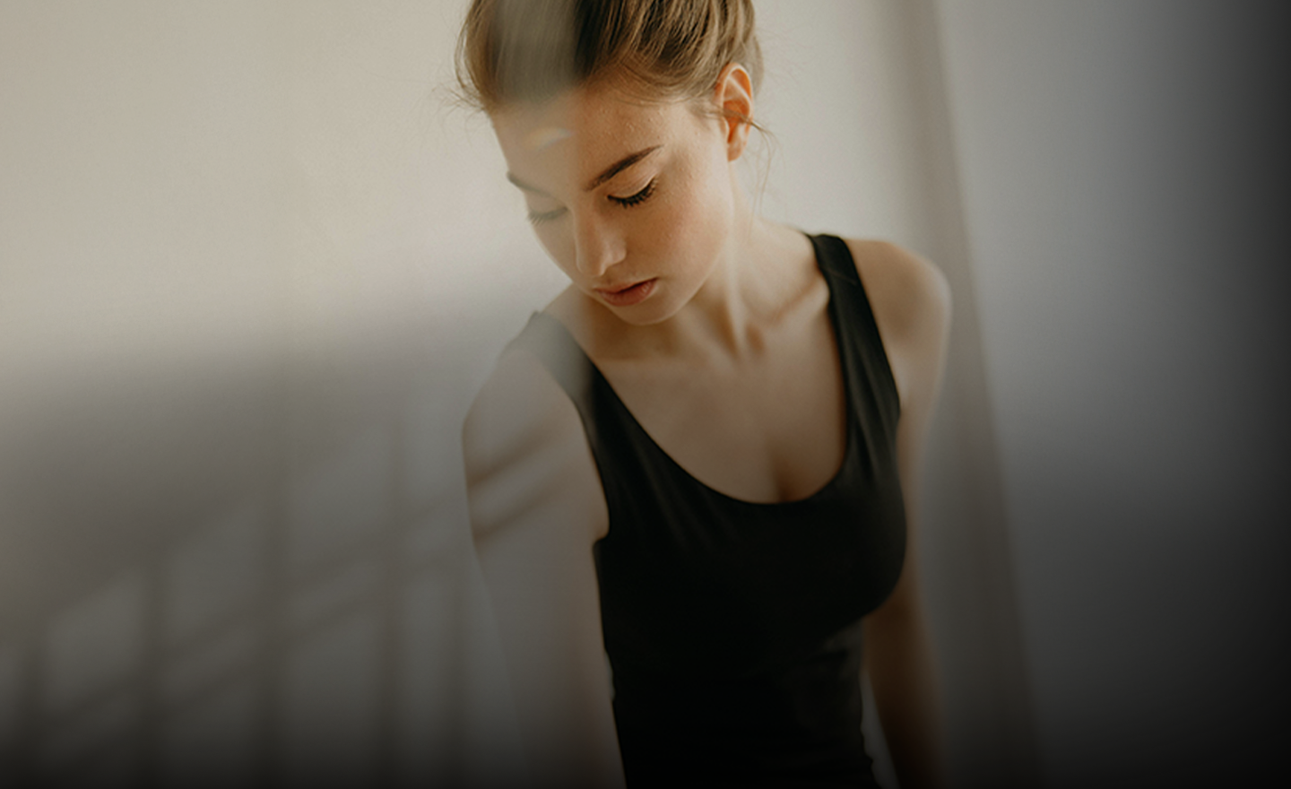 A woman in a black tank top looking down, with soft lighting highlighting her features.