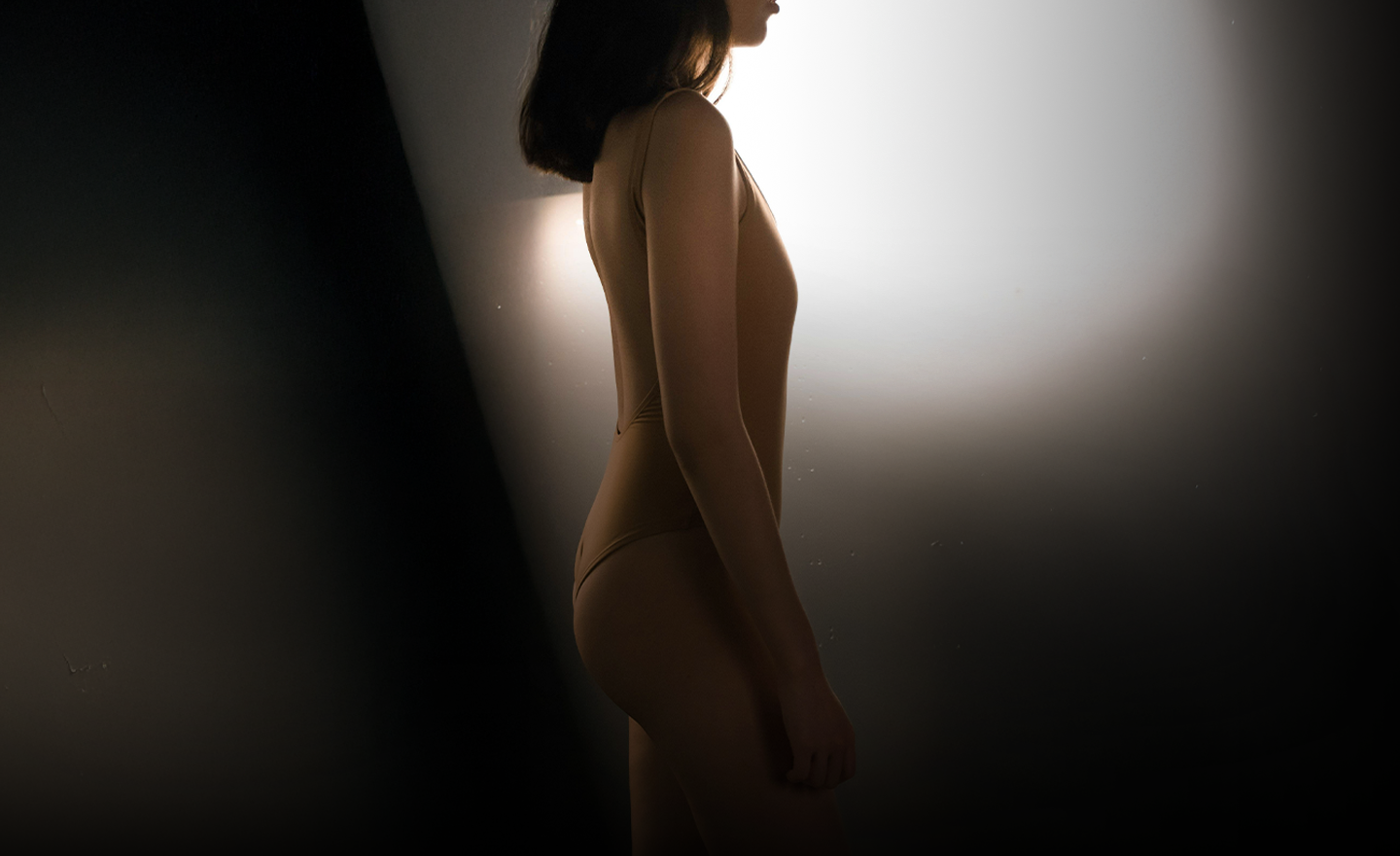 A silhouette of a woman in a fitted bodysuit standing sideways, showcasing a graceful profile.