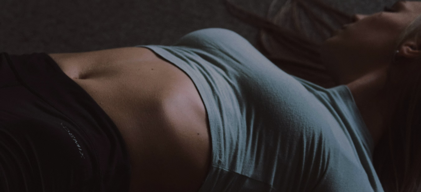 A woman lying down, dressed in a light blue top and dark leggings, with her hair partially covering her face.