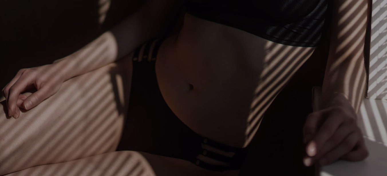 A person's lower torso wearing black lingerie, with light and shadow patterns created by horizontal stripes.