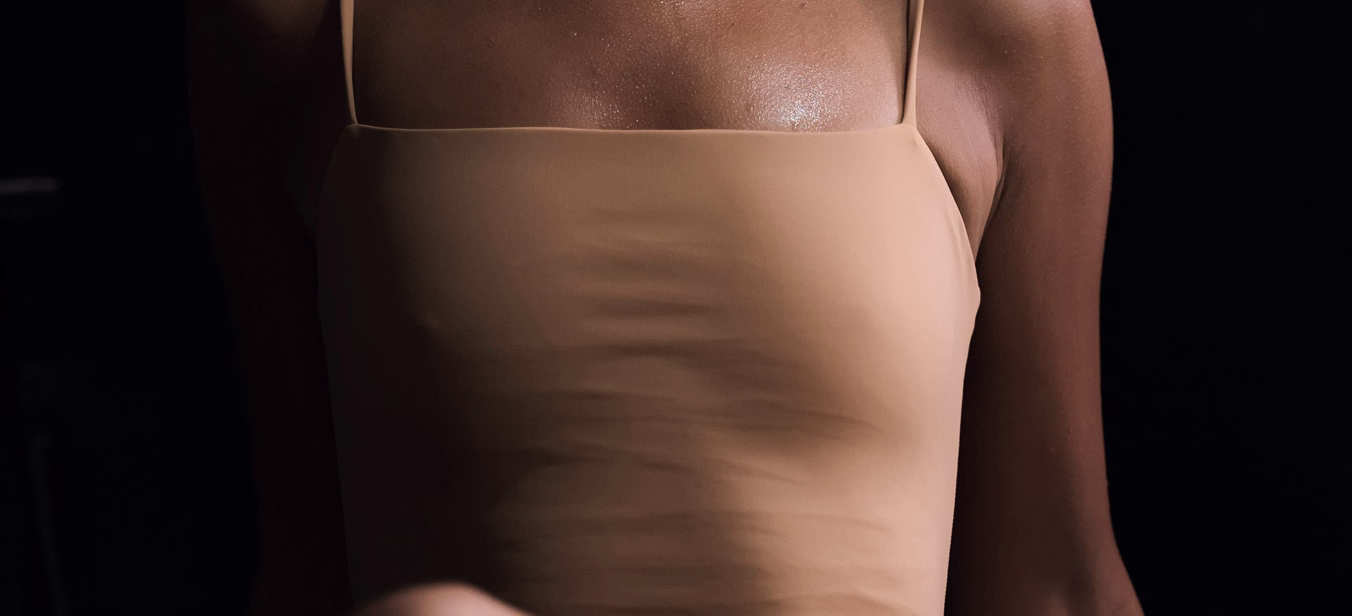 A close-up of a person wearing a light beige spaghetti strap top, showing the upper part of their torso and shoulder.