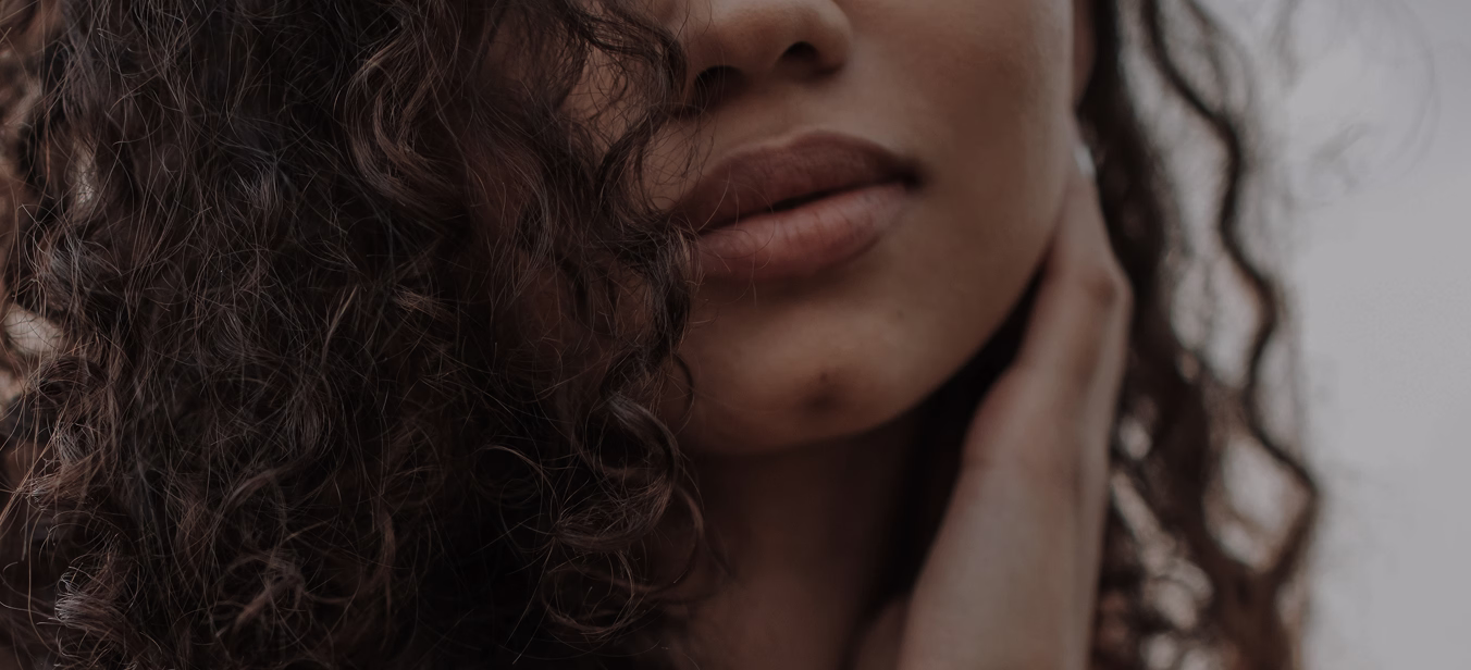 A close-up of a woman's face with curly hair, focusing on her lips and chin.