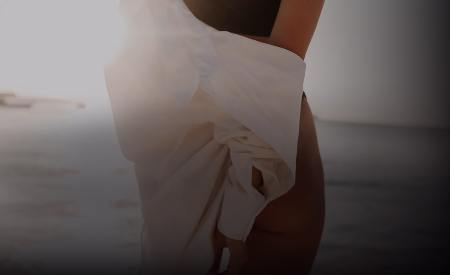 A person holding a white shirt while standing in shallow water, with bright sunlight illuminating the scene.