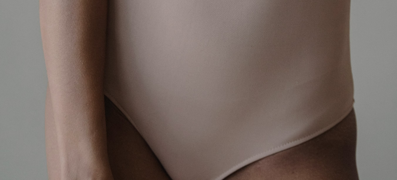 A close-up view of a person's torso wearing a beige one-piece swimsuit.