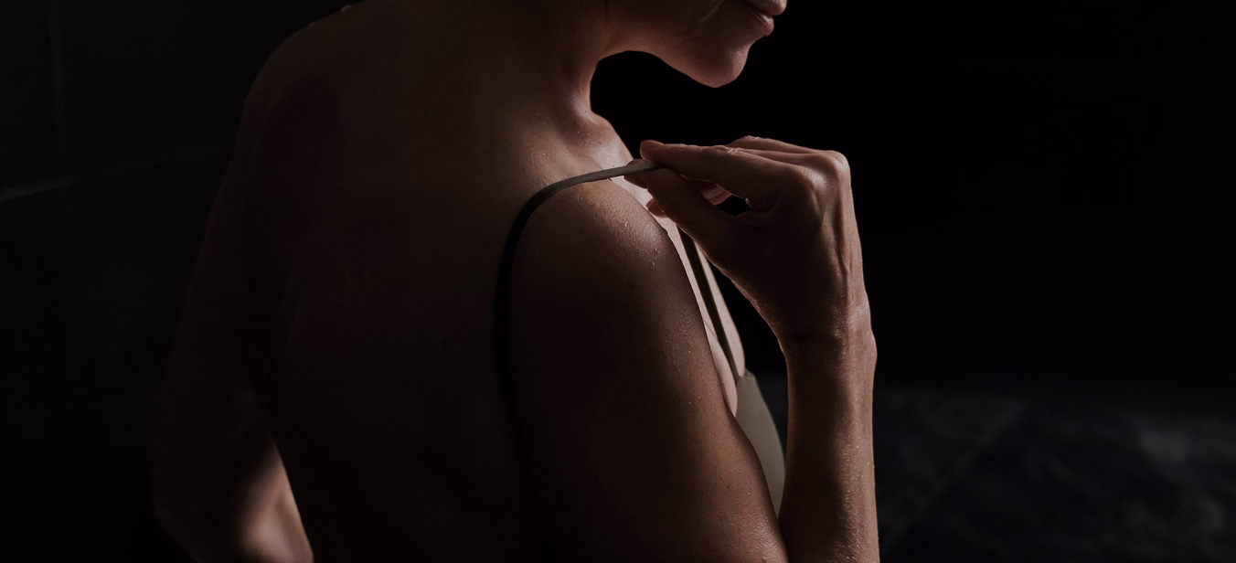 A woman adjusting the strap of a garment, with her back partially visible.