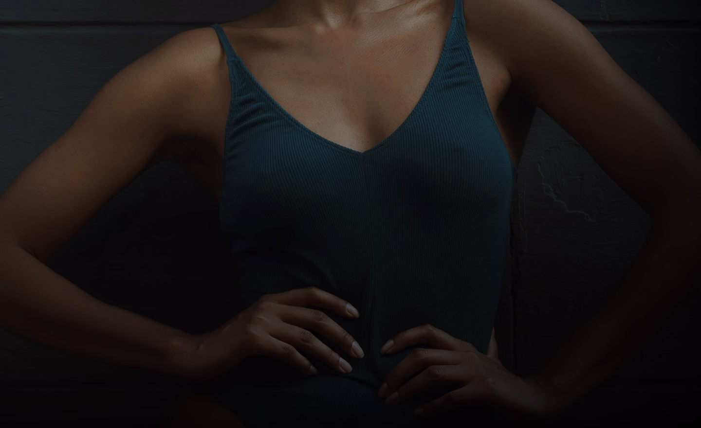 A model wearing a teal swimsuit, with hands placed on her hips, showcasing a confident pose.