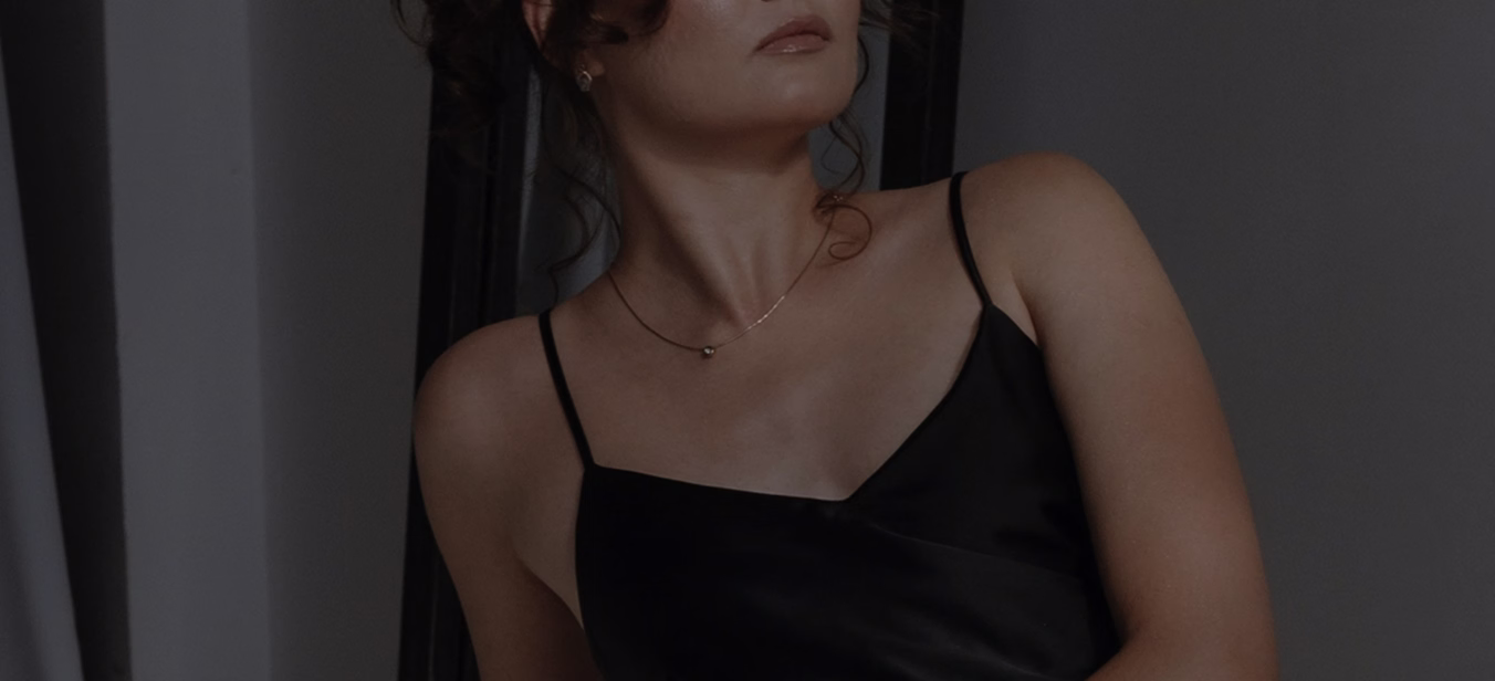 A woman with curly hair styled elegantly, wearing a black camisole top, looking slightly to her right with an introspective expression.