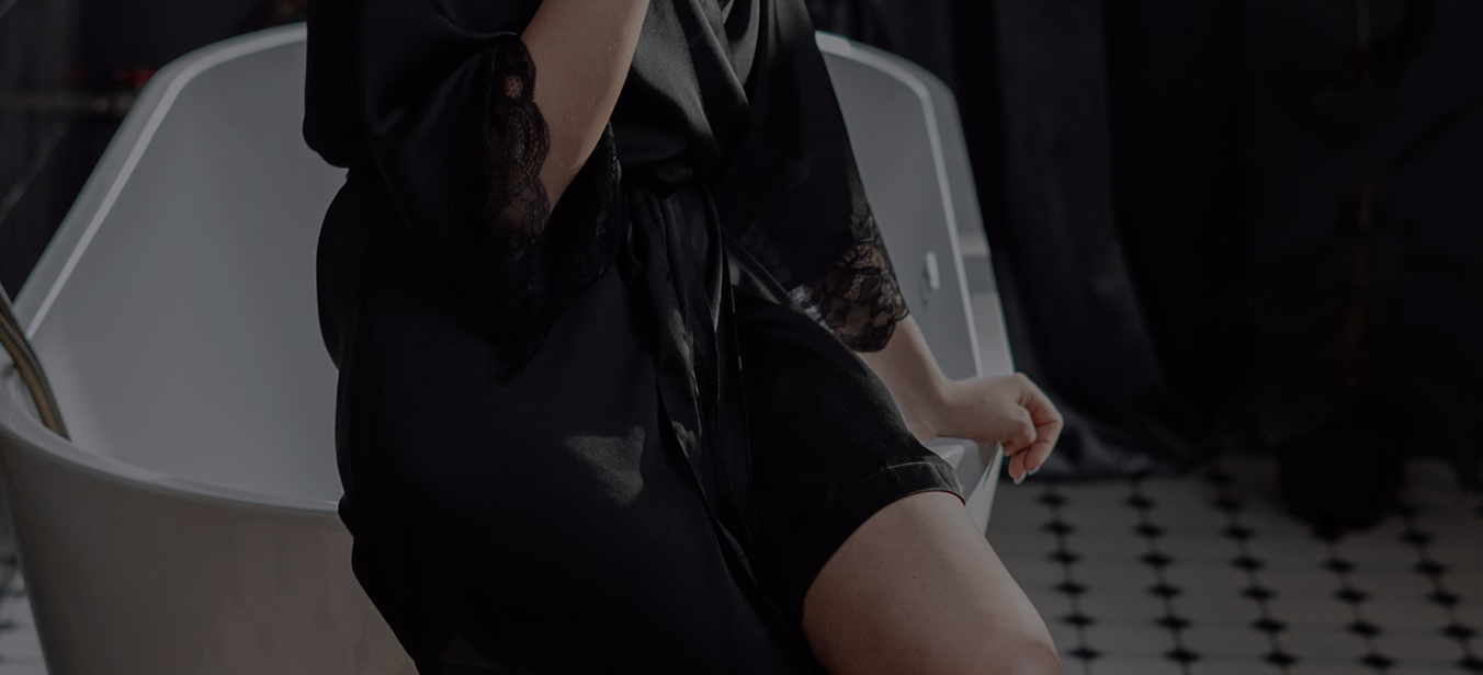A person wearing a black robe with lace detailing, seated in a modern, minimalist environment, appearing thoughtful or reflective.