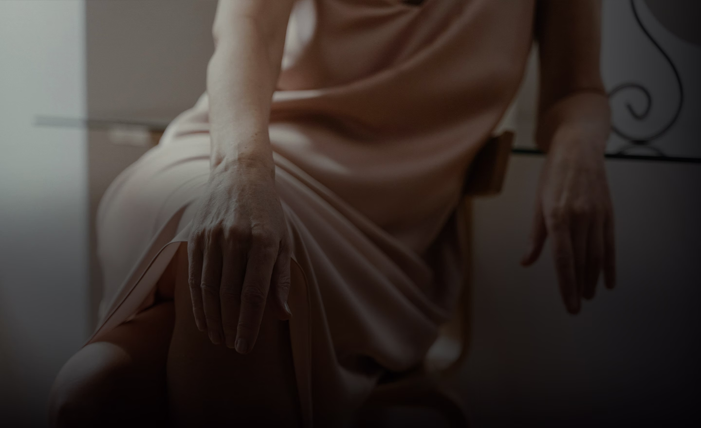 A close-up of a woman's hand resting gently on her thigh, wearing a soft, flowing dress.