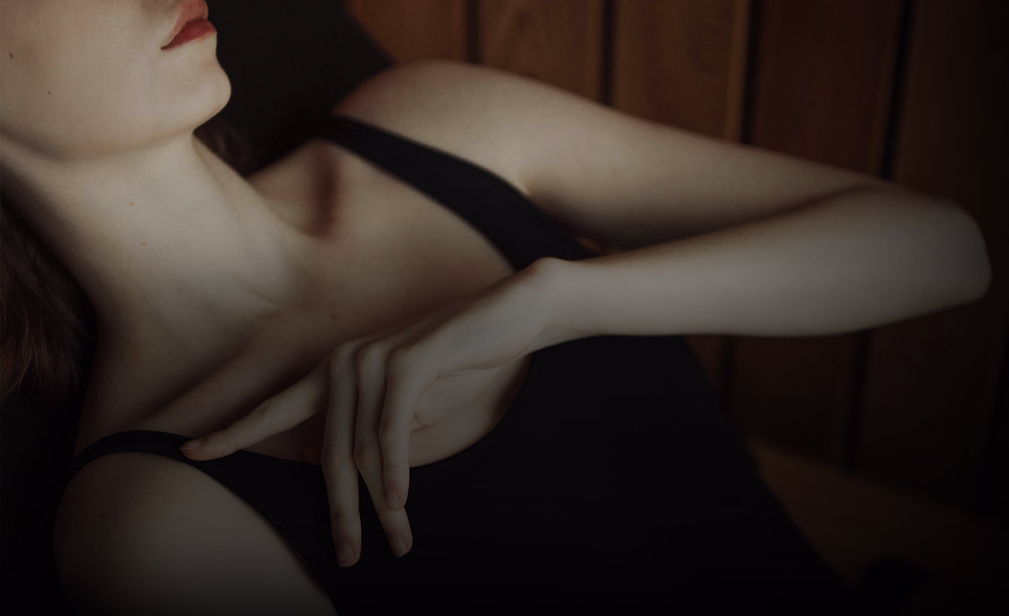 A close-up of a person in a black tank top resting their hand on their shoulder, with a focus on the neckline and hand position.