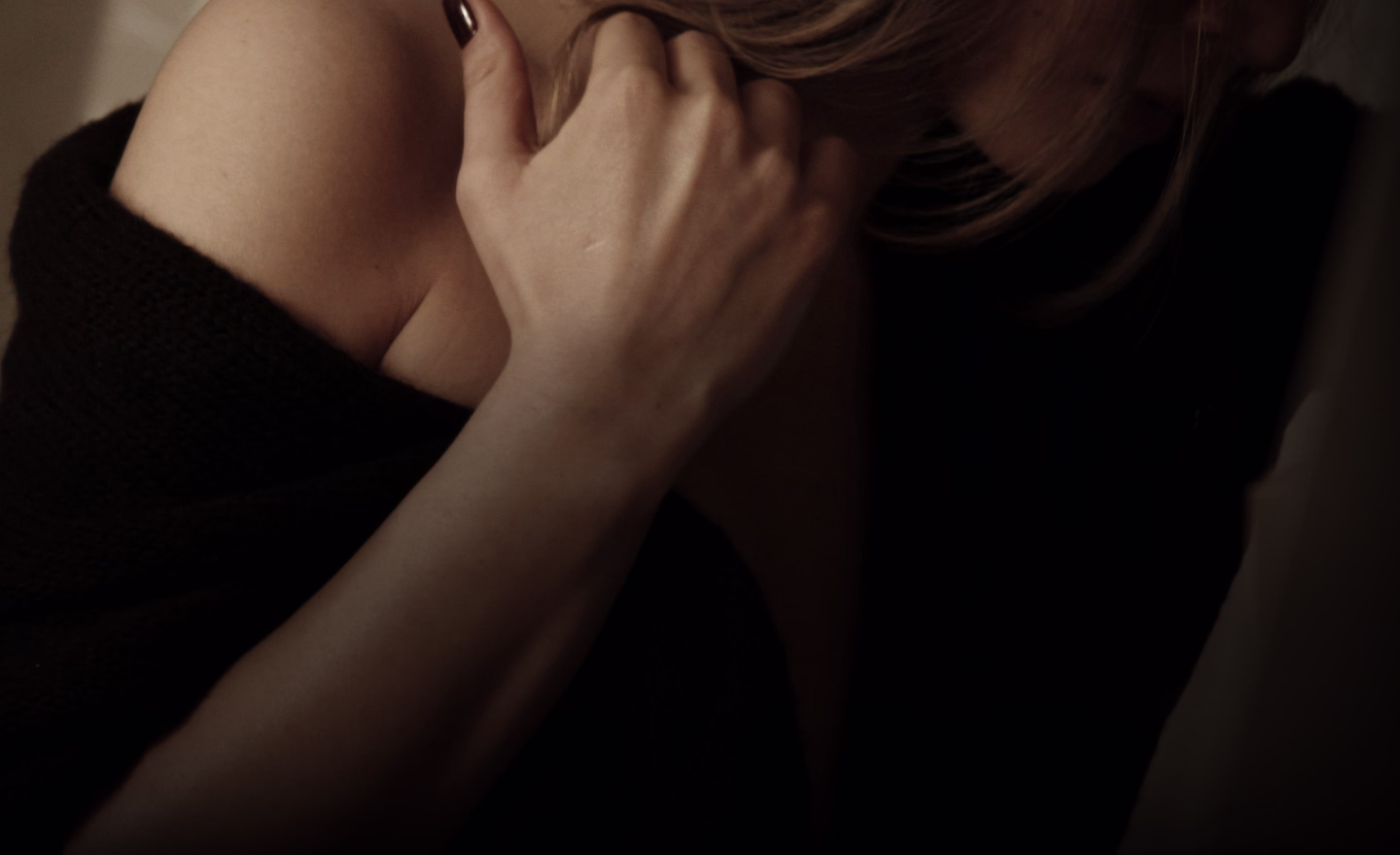 A close-up of a woman's shoulder and hand, with her hair partially obscuring her face, conveying a sense of intimacy and softness.