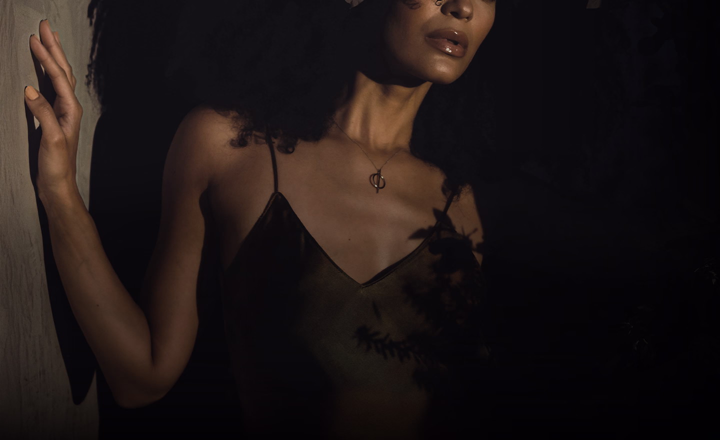 A woman with curly hair wearing a simple necklace featuring a circular pendant, with her shoulders partially visible.