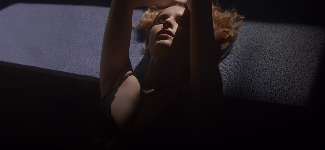 A model posing with her arms raised, wearing black lingerie, and with soft, highlight lighting emphasizing her facial features.
