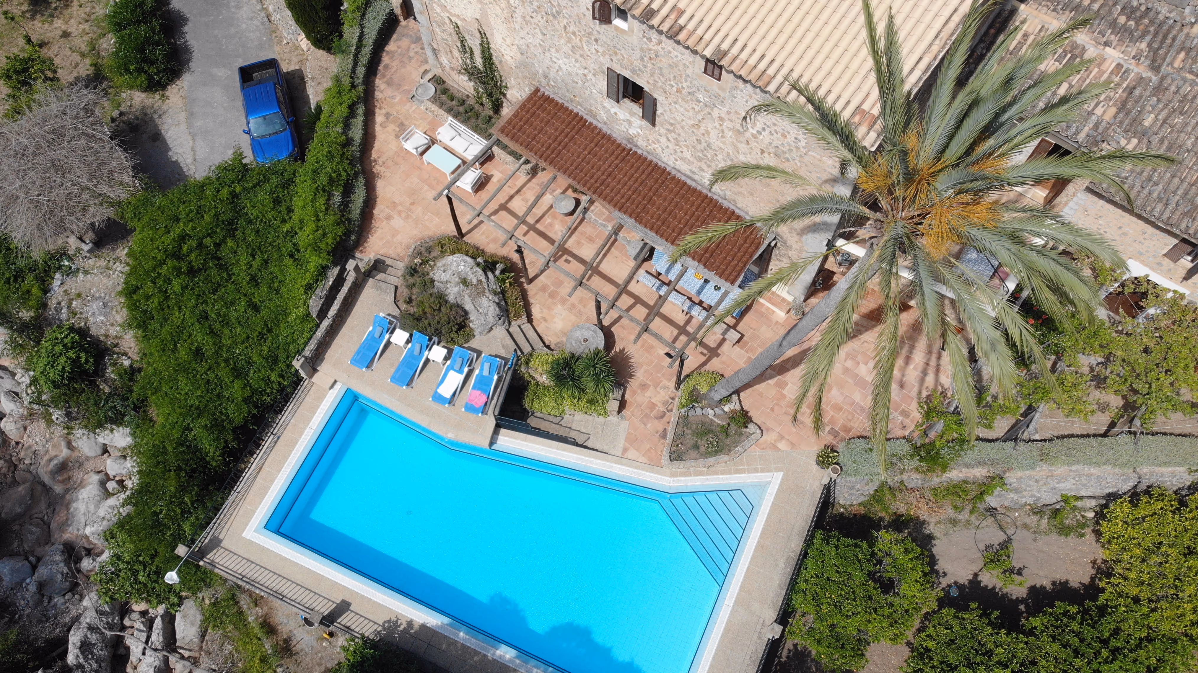 Aerial view of Finca Higo’s pool area with sun loungers, palm trees, and shaded seating in a Mediterranean garden.