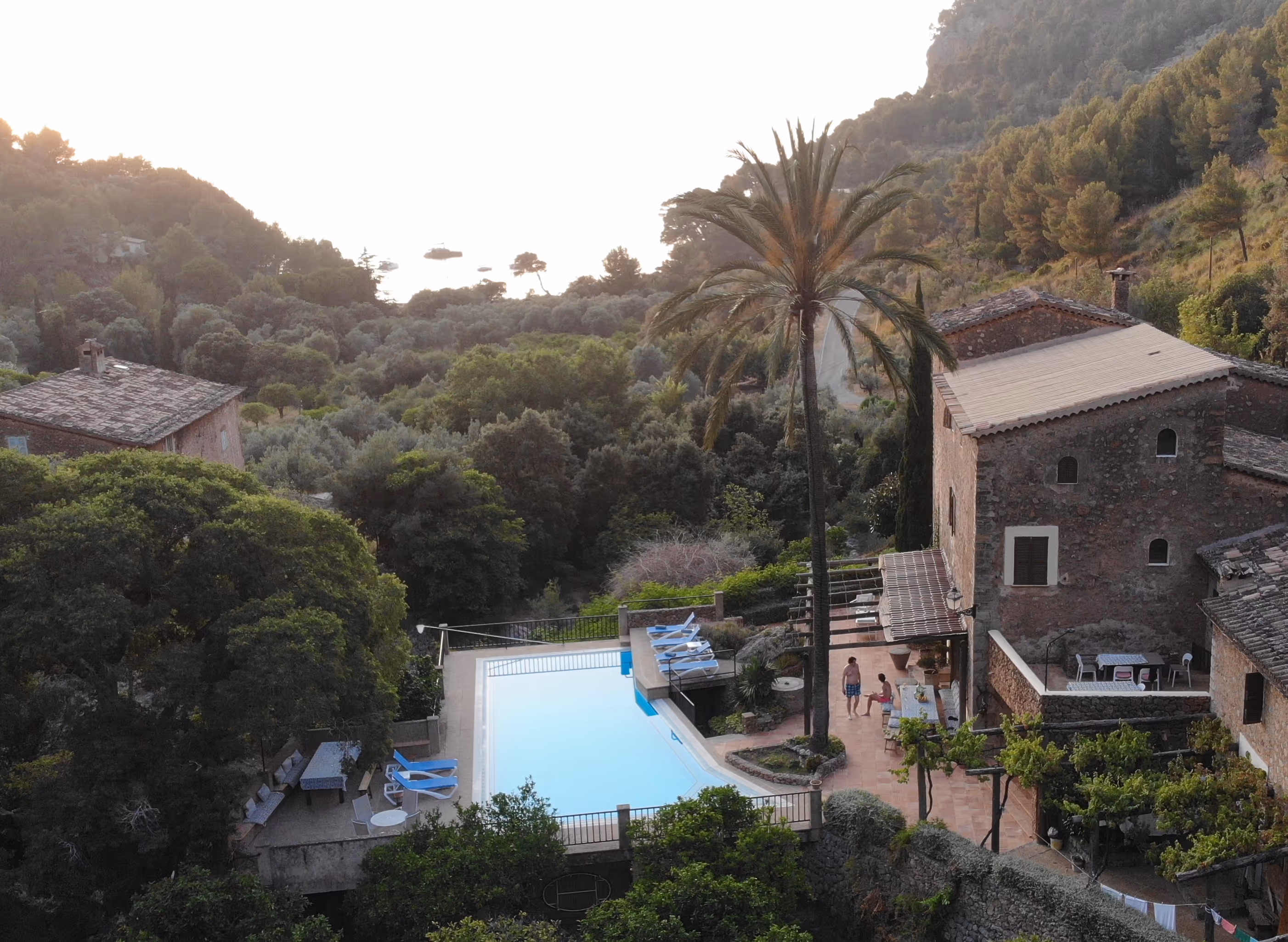 View of Finca Higo overlooking Cala Tuent at sunset, with two yoga participants standing near the pool.