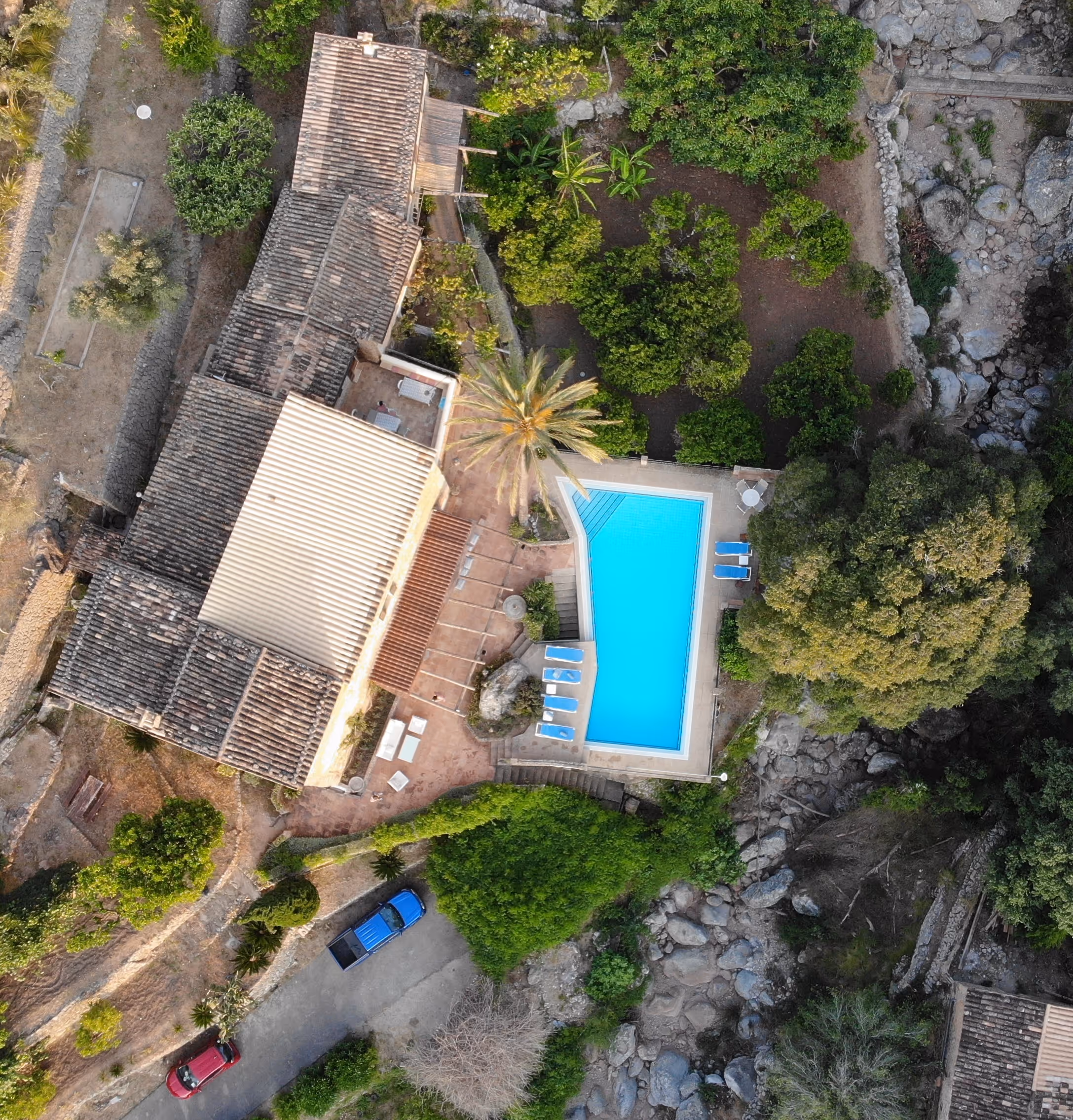Top-down aerial of the pool and stone buildings at Finca Higo, framed by terraced paths and natural rock formations.