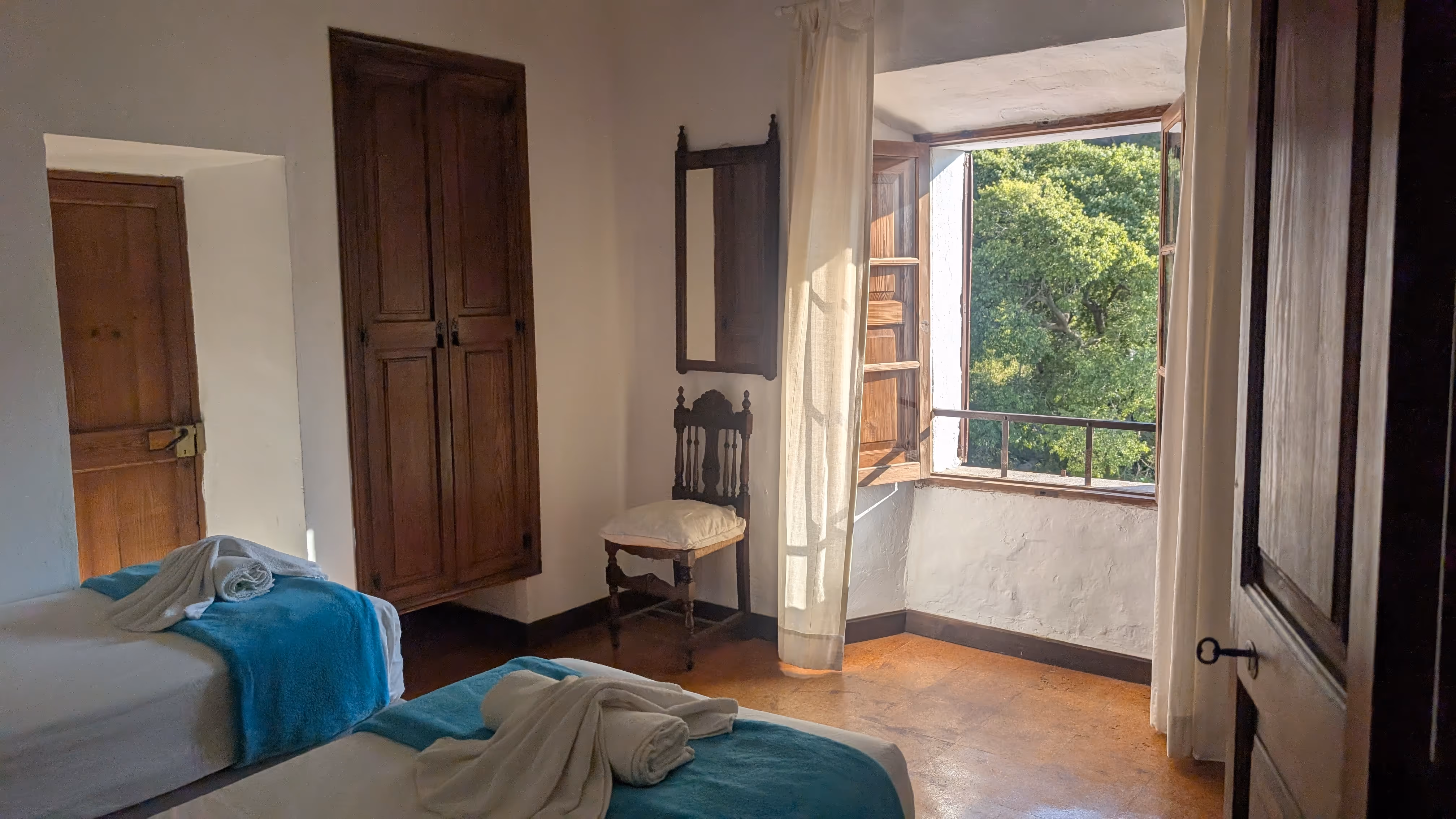 ustic guest room with wooden furniture and a large window offering scenic views of trees and mountains.