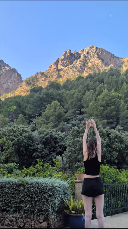Woman practicing yoga outdoors in front of lush greenery and rocky mountain peaks at the Finca Higo retreat.