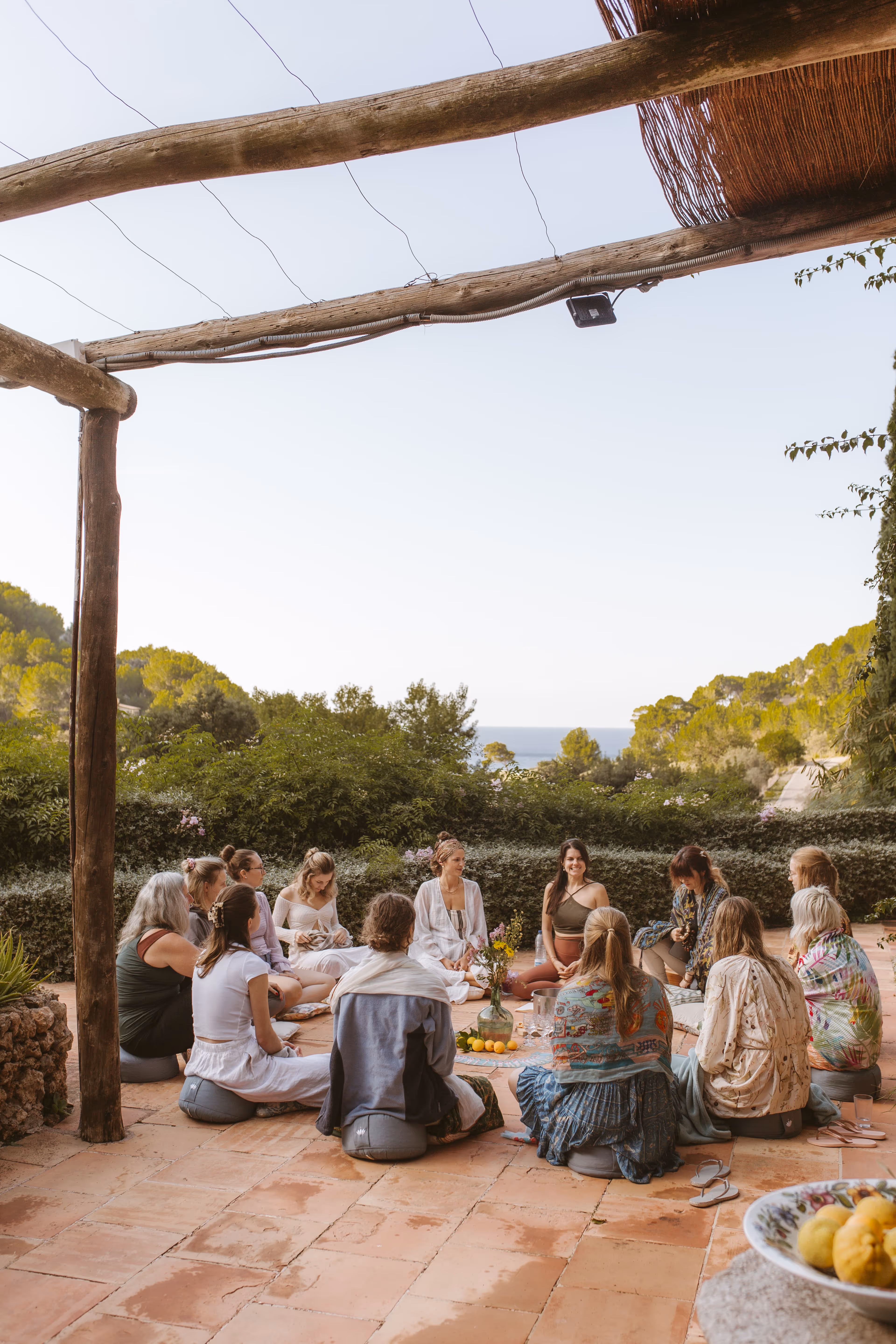 Yoga group sitting in a circle outdoors at Finca Higo, with views of the beach and surrounding nature in the background.