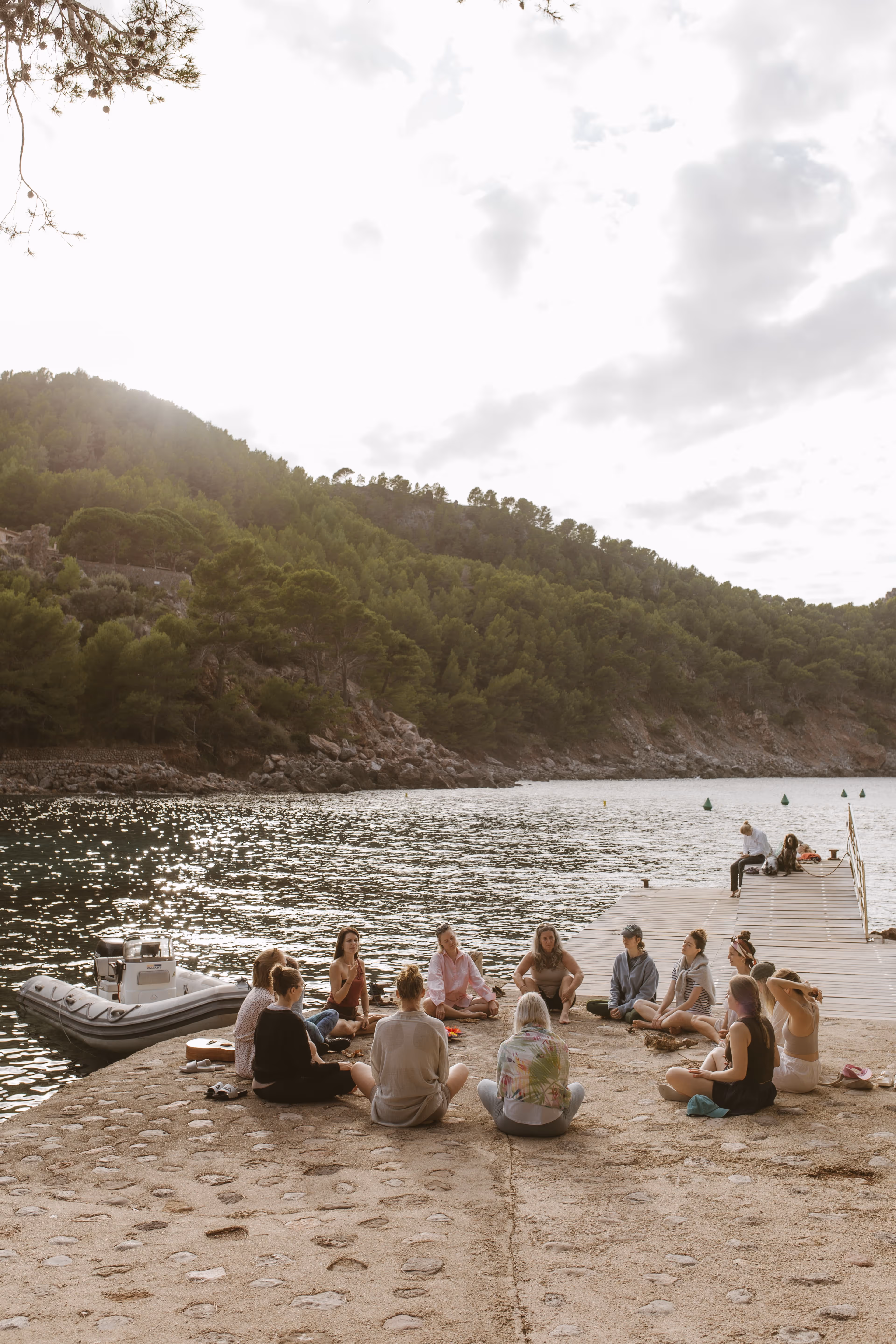Finca Higo retreat participants sitting in a circle on the shore of Cala Tuent in Mallorca, reflecting by the water.