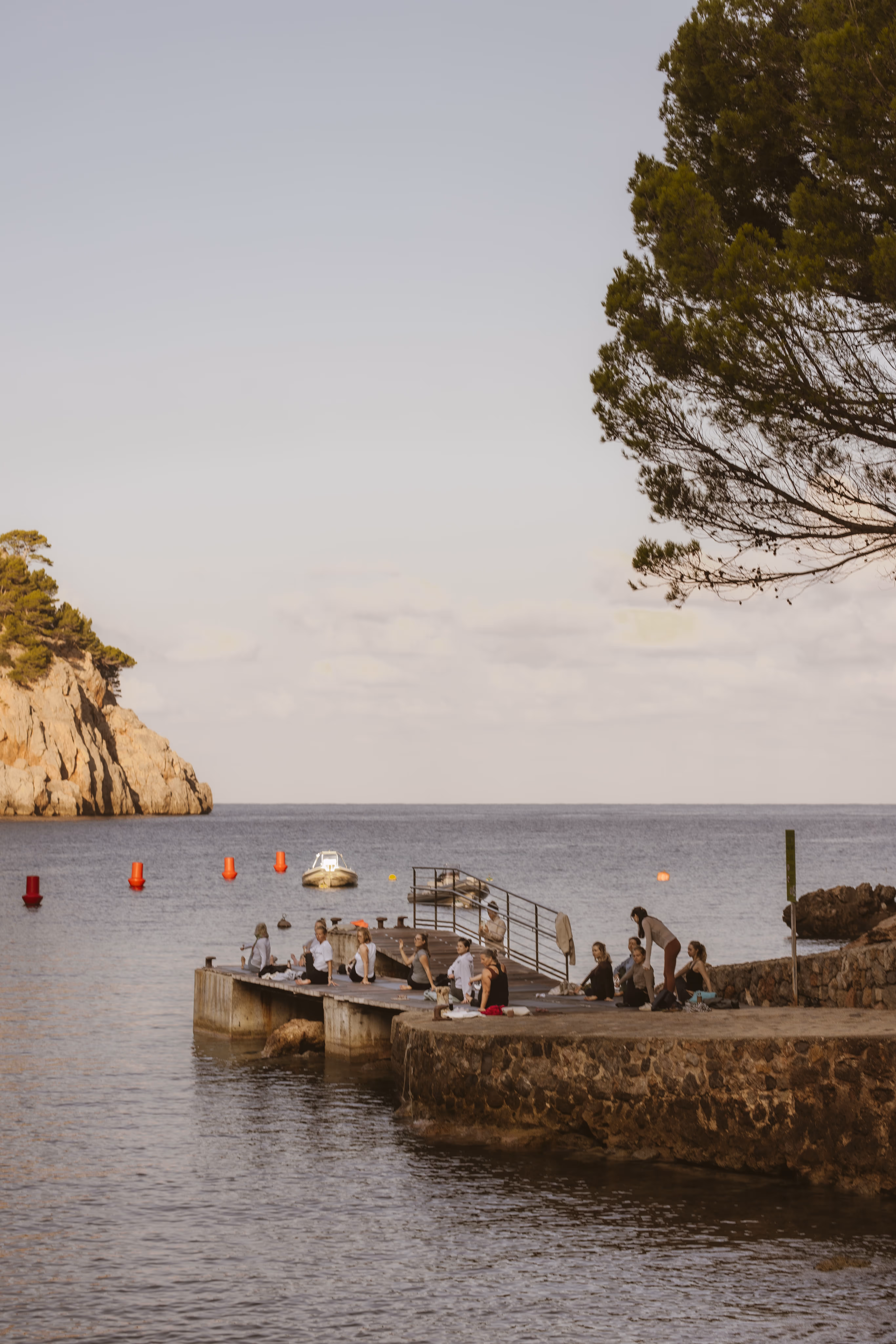 Retreat participants gathering on a stone pier at Cala Tuent, overlooking the calm Mediterranean Sea.