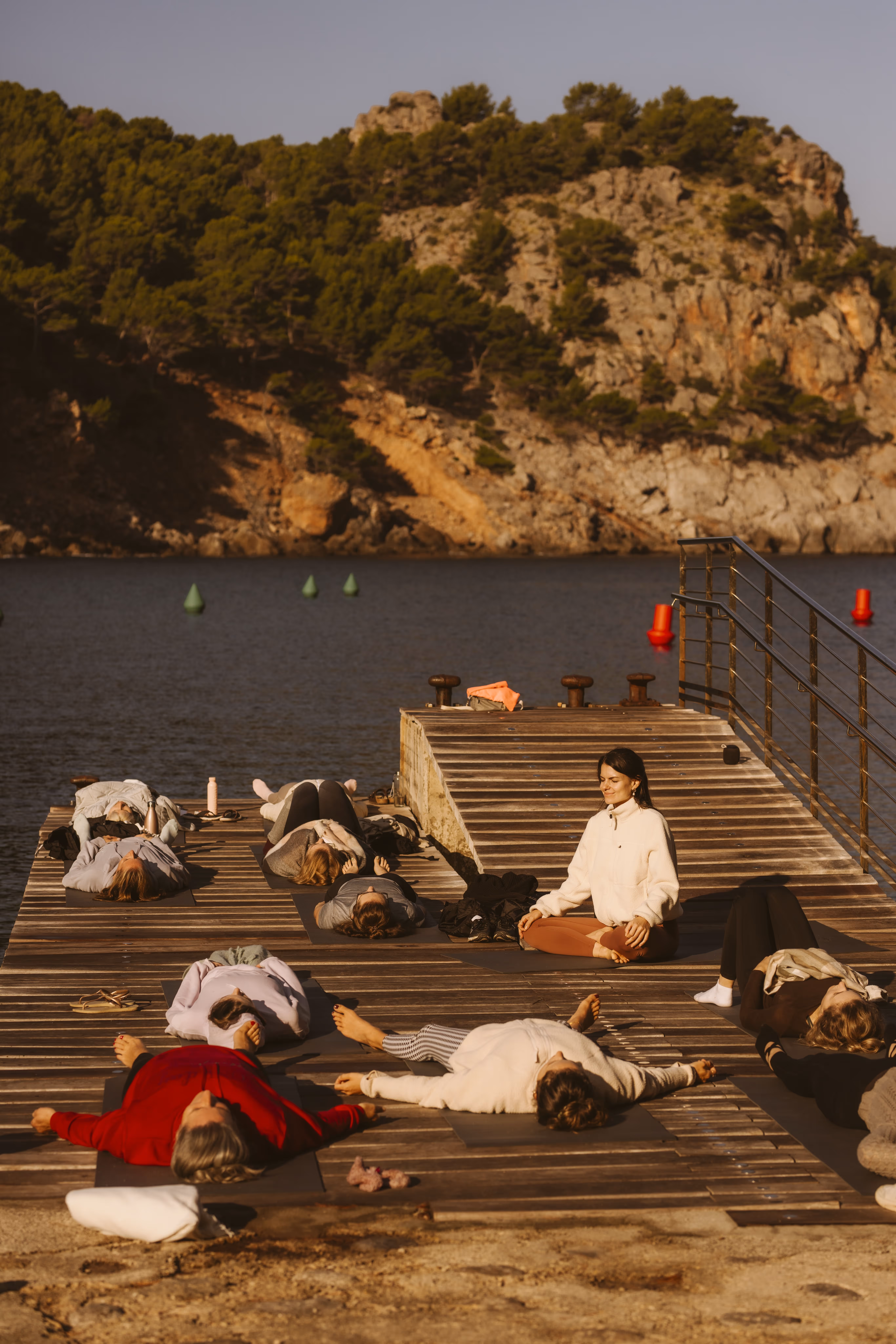 Yoga participants practicing gentle exercises on a pier by the sea at sunset in Cala Tuent.Yoga participants practicing gentle exercises on a pier by the sea at sunset in Cala Tuent.