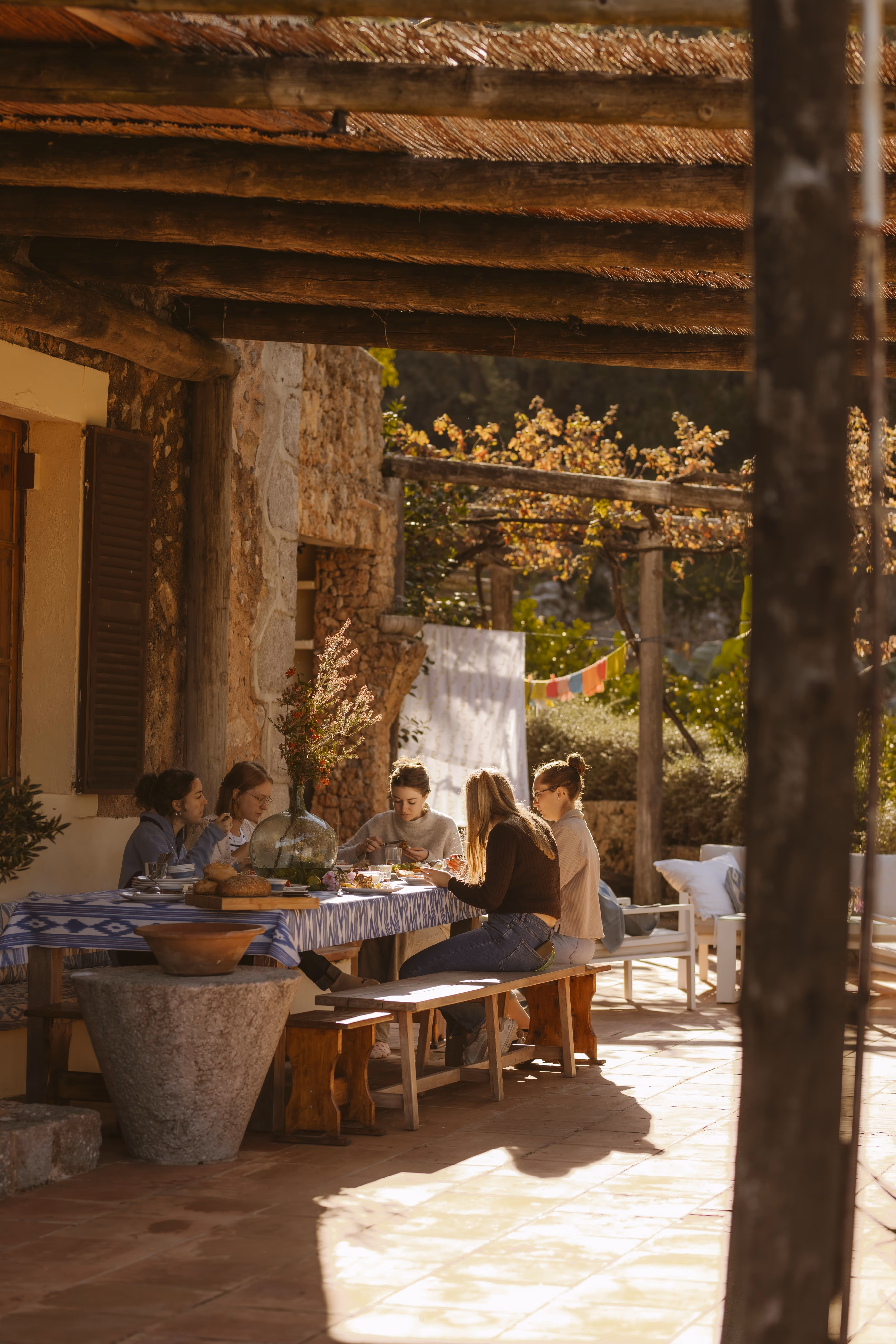 Small group enjoying a meal together outdoors under a shaded terrace roof.