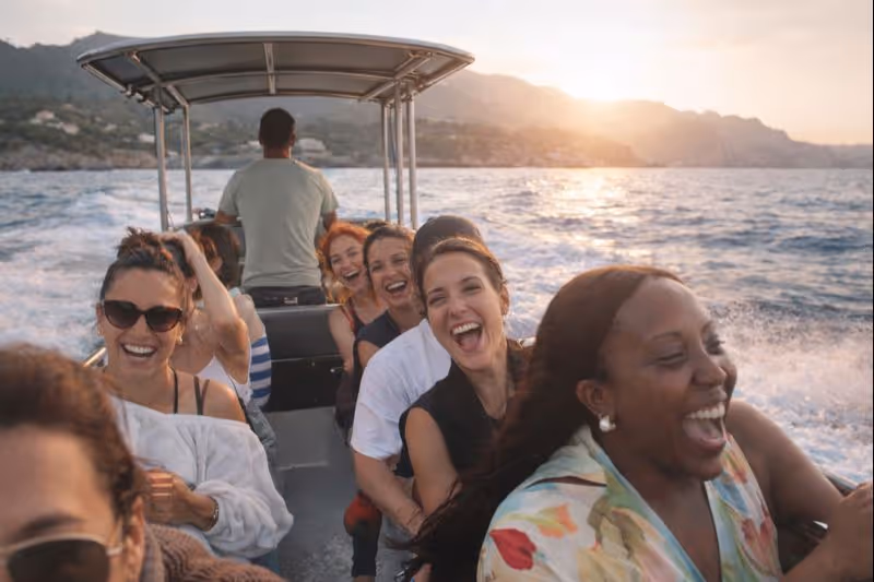 Women laughing while riding a boat taxi along the coast of Mallorca at sunset.