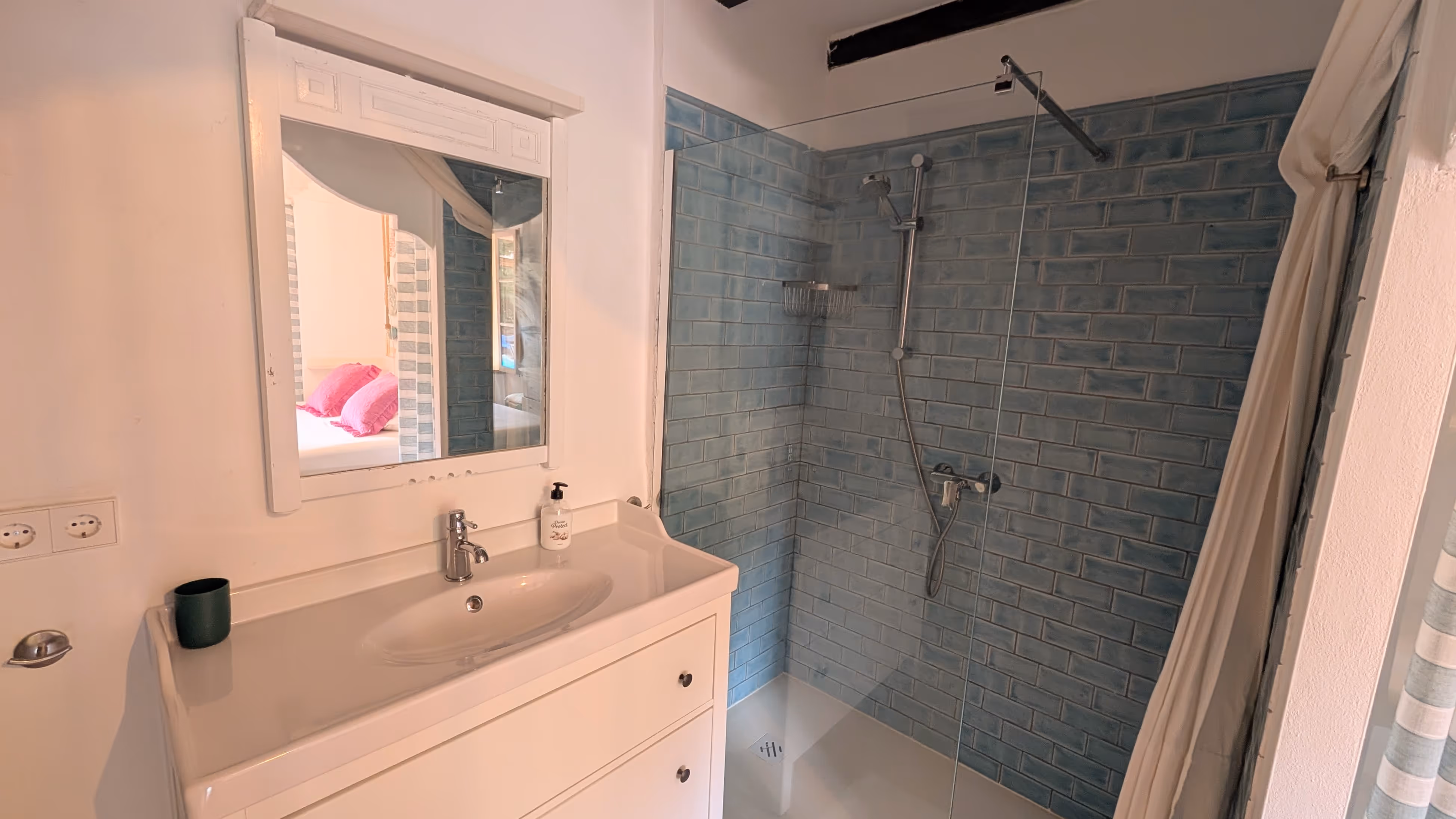 Modern bathroom with a walk-in shower tiled in blue, featuring a white sink and mirror.