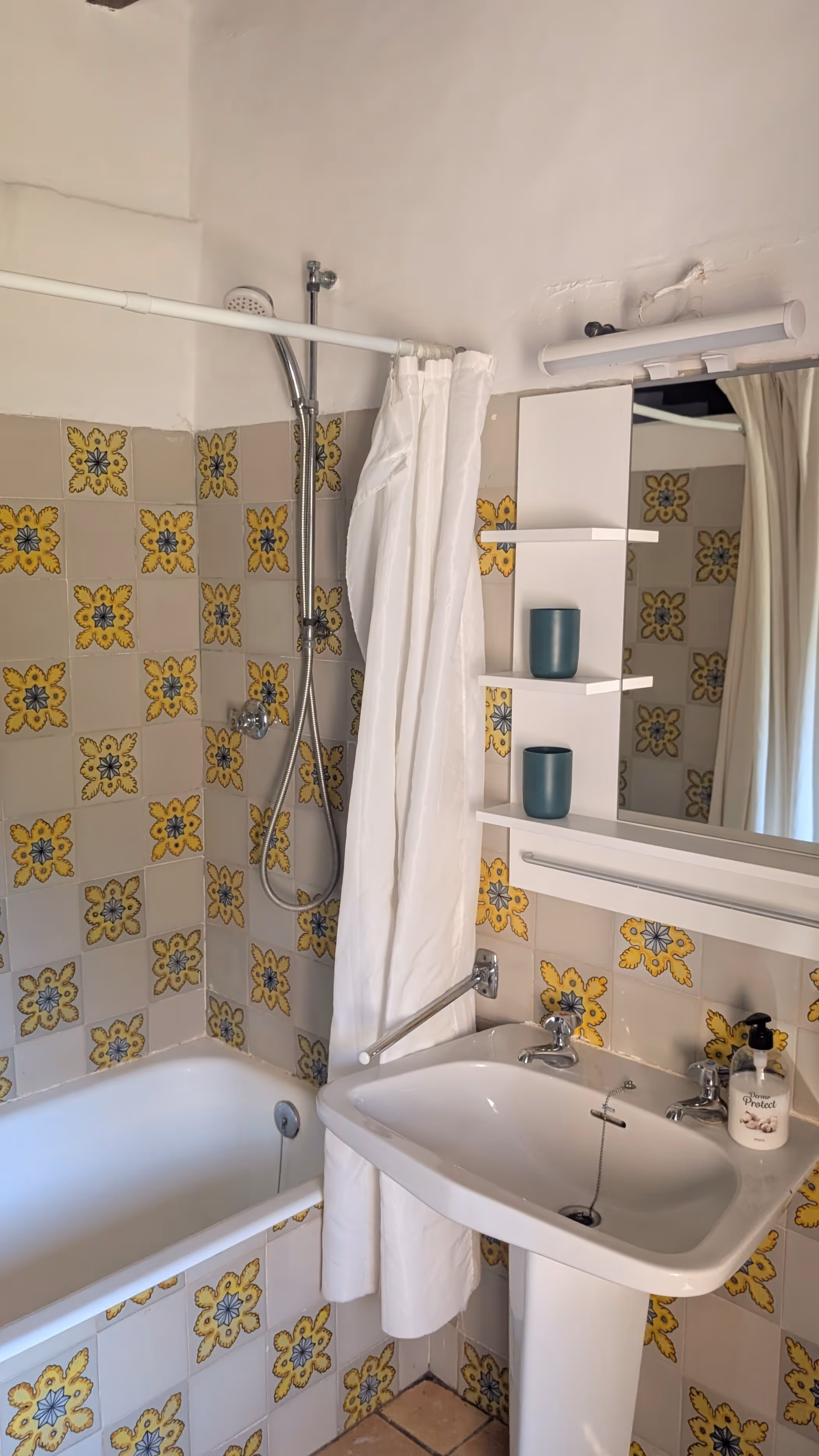 Traditional bathroom with patterned yellow-and-blue tiles, a bathtub with shower curtain and a white sink with mirror.
