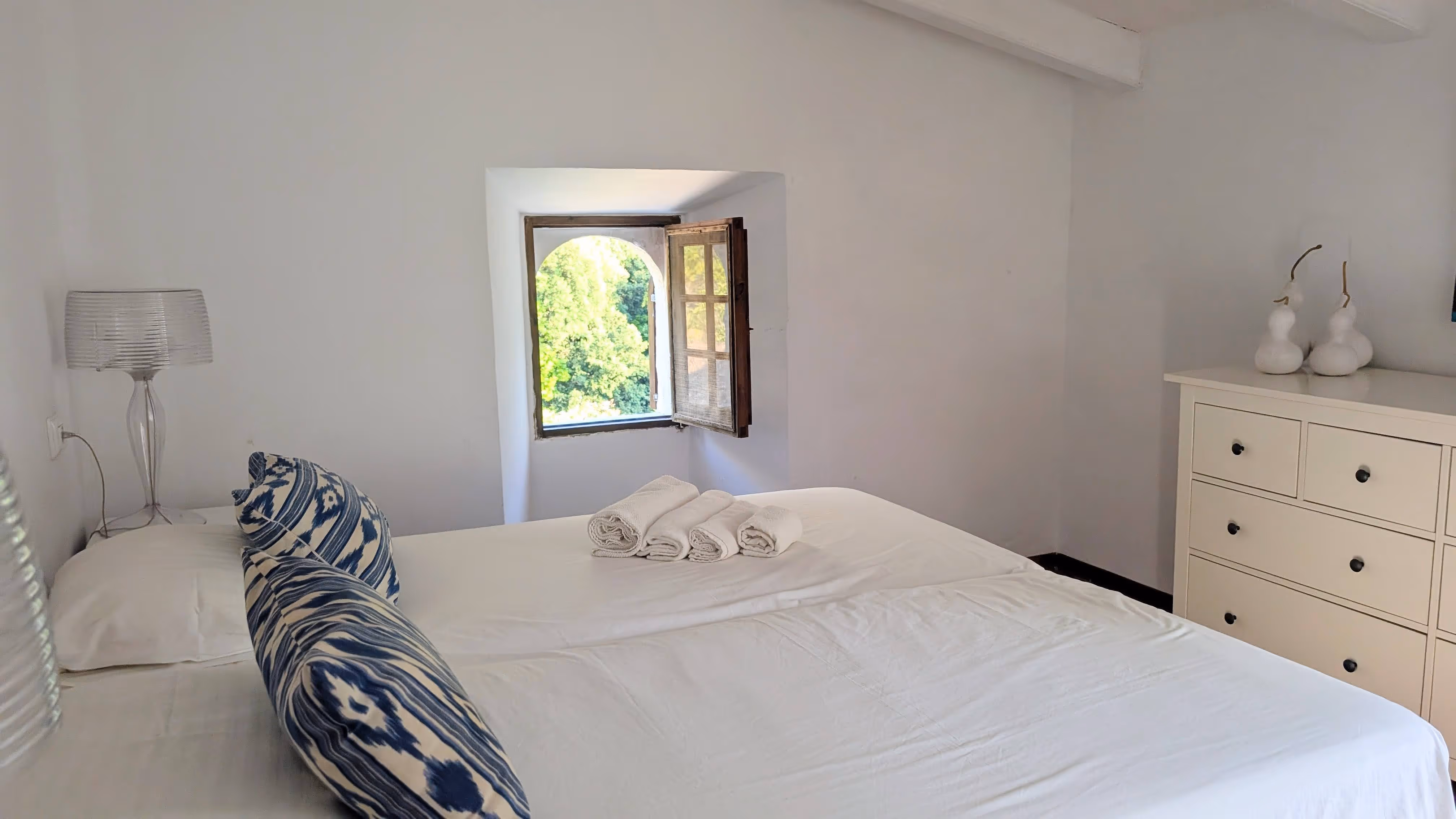 Double room with prepared towels, wooden beams, and a small window overlooking the mountains.