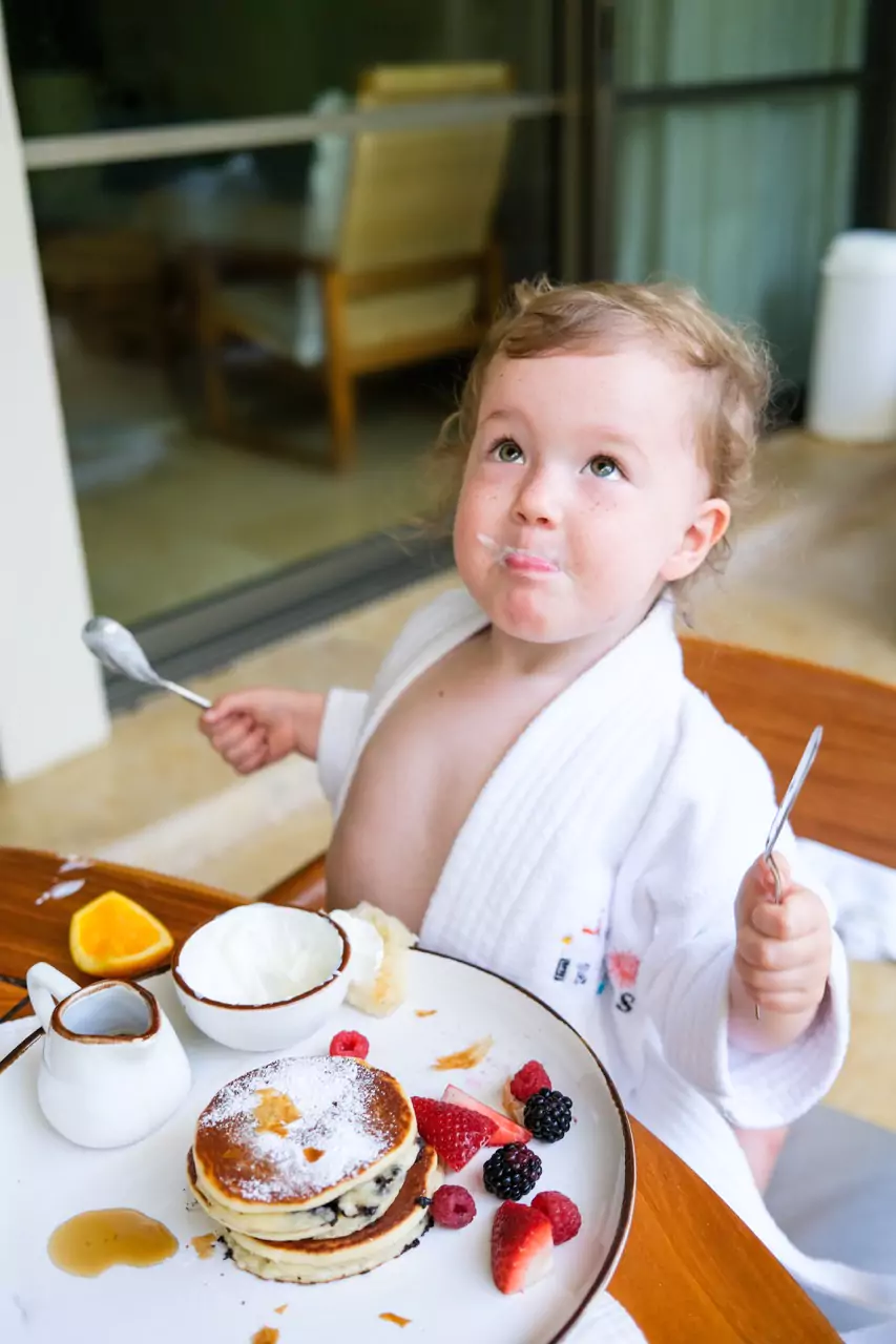 A toddler eating breakfast in a robe at Rosewood Mayakoba
