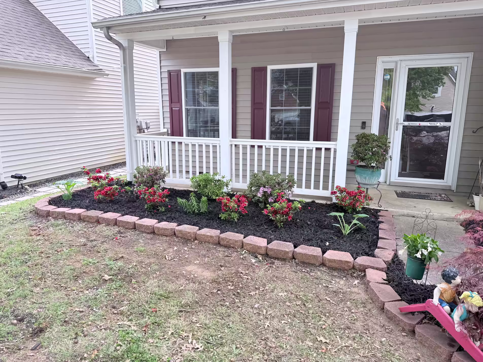 Small garden in front of a house with mulch and bricks.