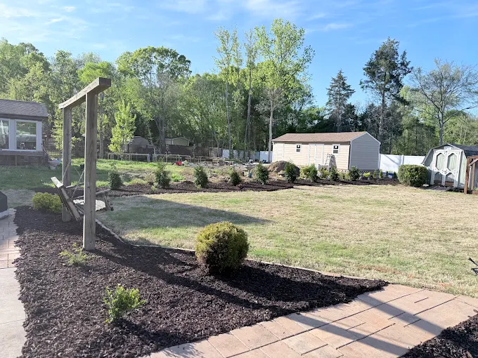 Backyard design with mulch, swings, hardscaping, and grass.