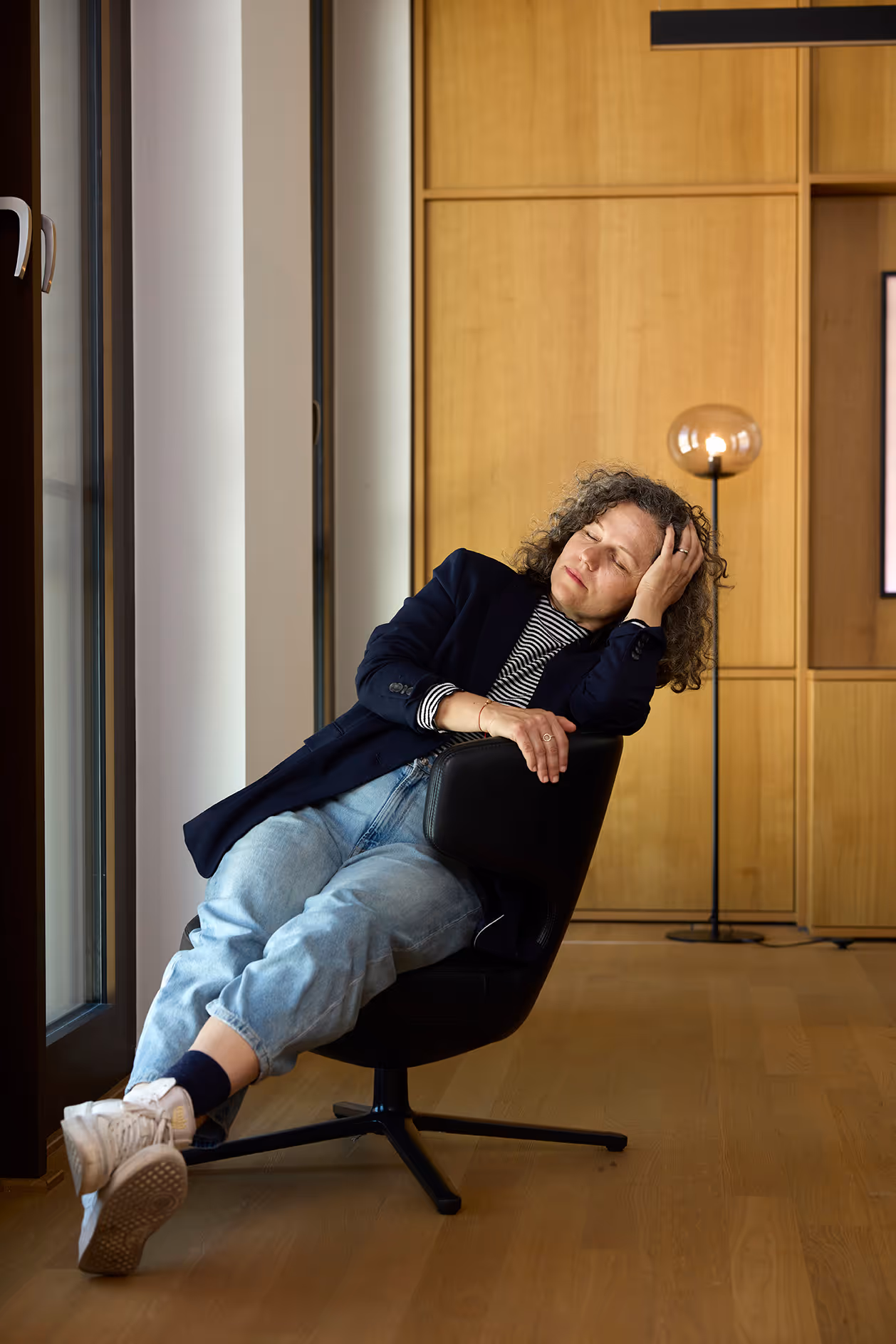 Person mit Locken sitzt entspannt im Sessel, lehnt sich zurück und schließt die Augen.
