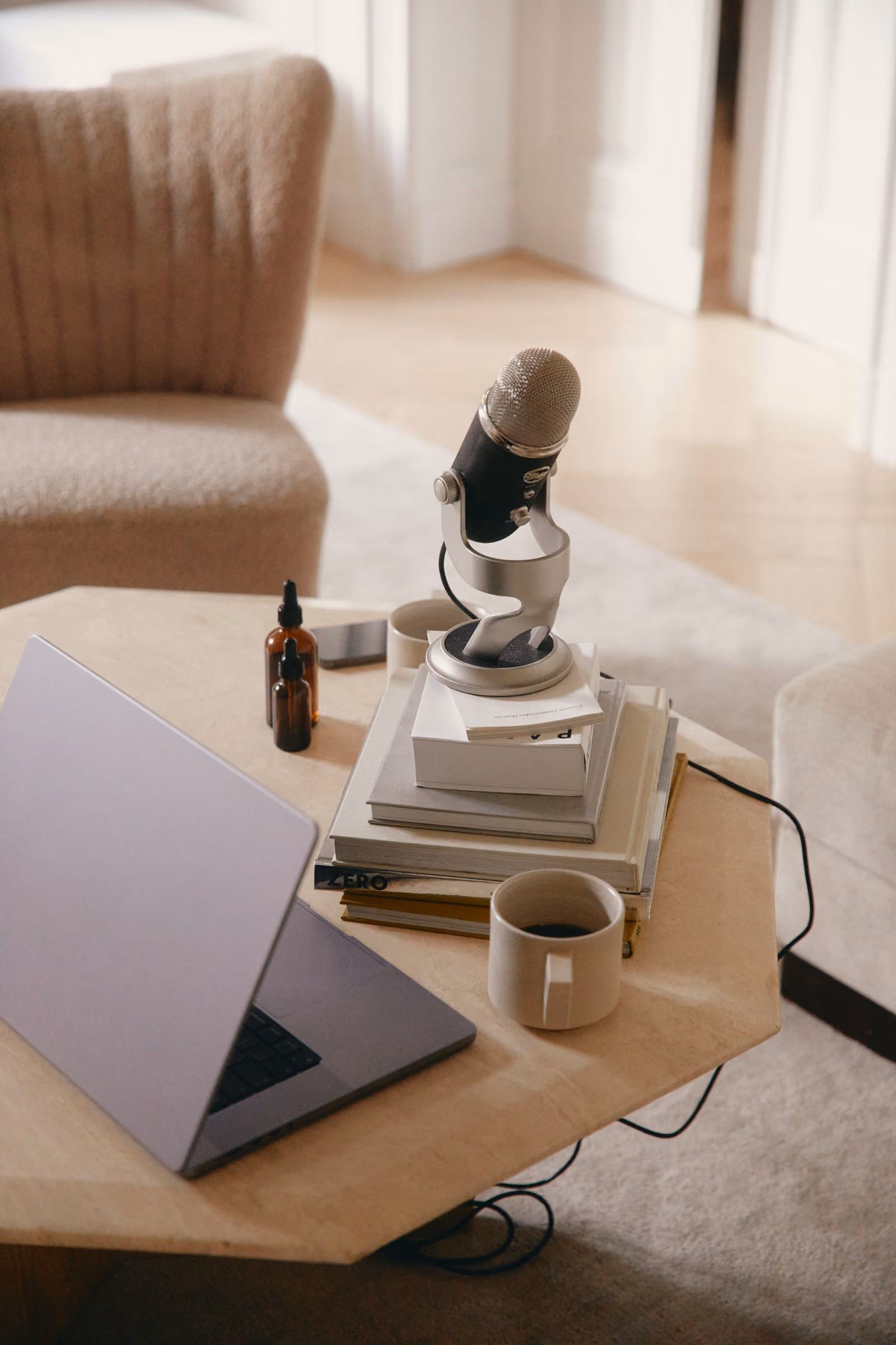 Laptop, Stapel Bücher und Mikrofon auf einem Tisch mit Tasse Kaffee in einem gemütlichen Raum.