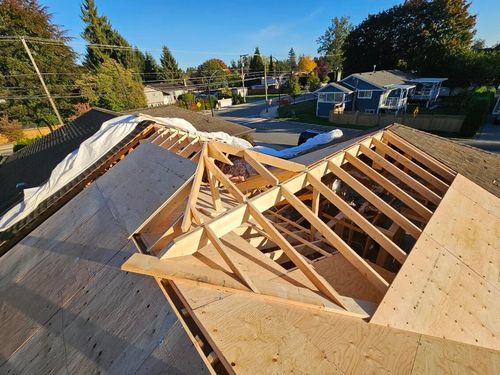 Partially constructed wooden roof framing on a house under a clear blue sky in a residential neighborhood.