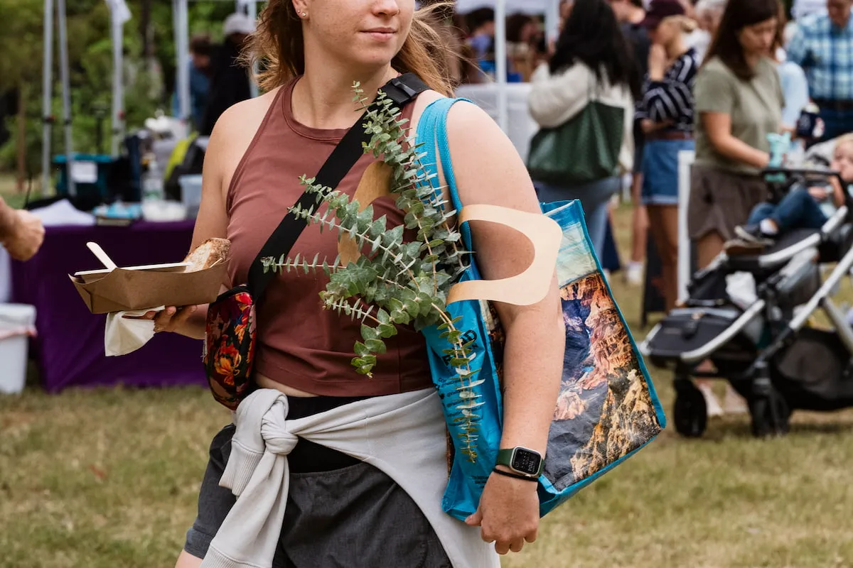 A woman walks through the market with a bag of local goods and a plate of delicious food.